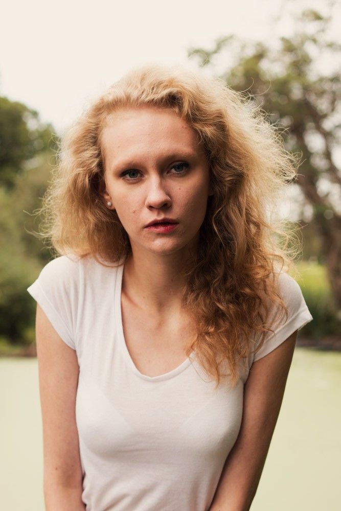 Portrait photography - Blonde woman with curly hair in white t-shirt posing outdoors in natural setting.