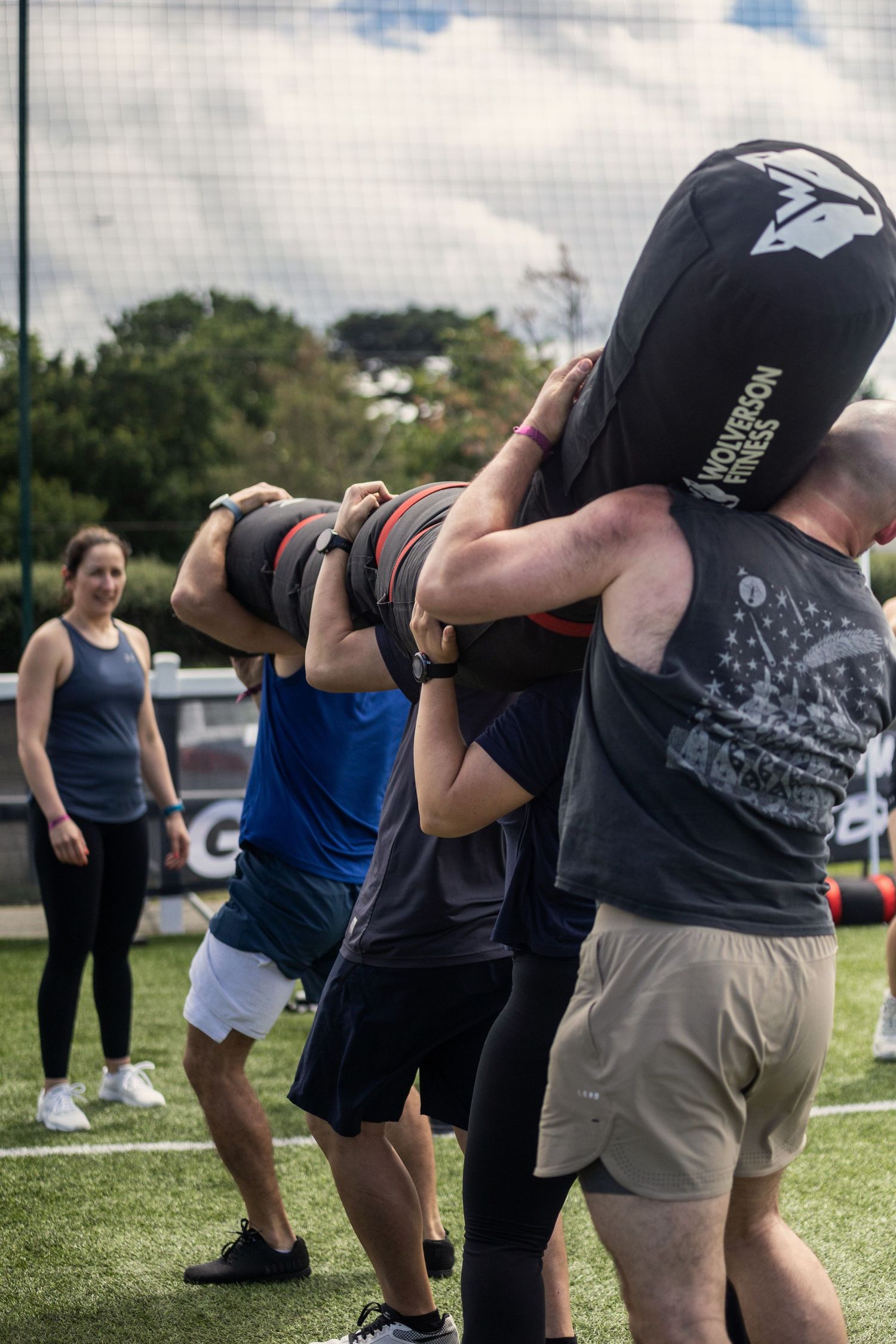 Group of participants lifting a heavy sandbag together during an outdoor team fitness challenge event.