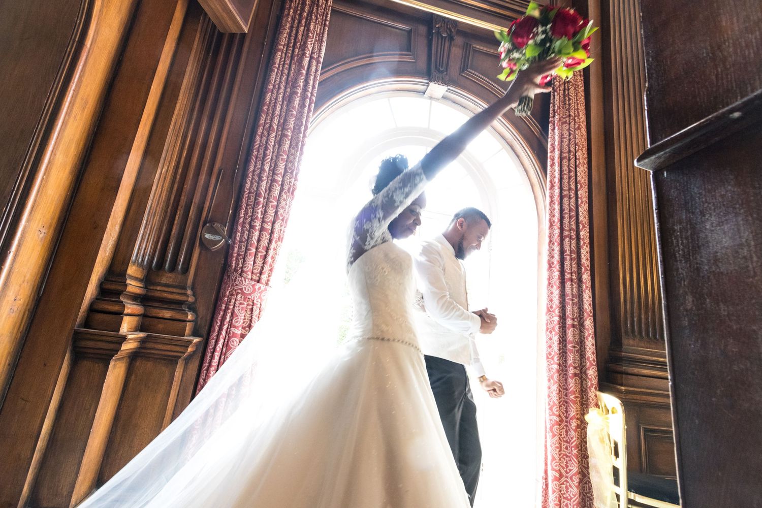 Wedding Photography - Bride and groom silhouetted in a grand arched doorway, bride holding a colorful bouquet aloft.