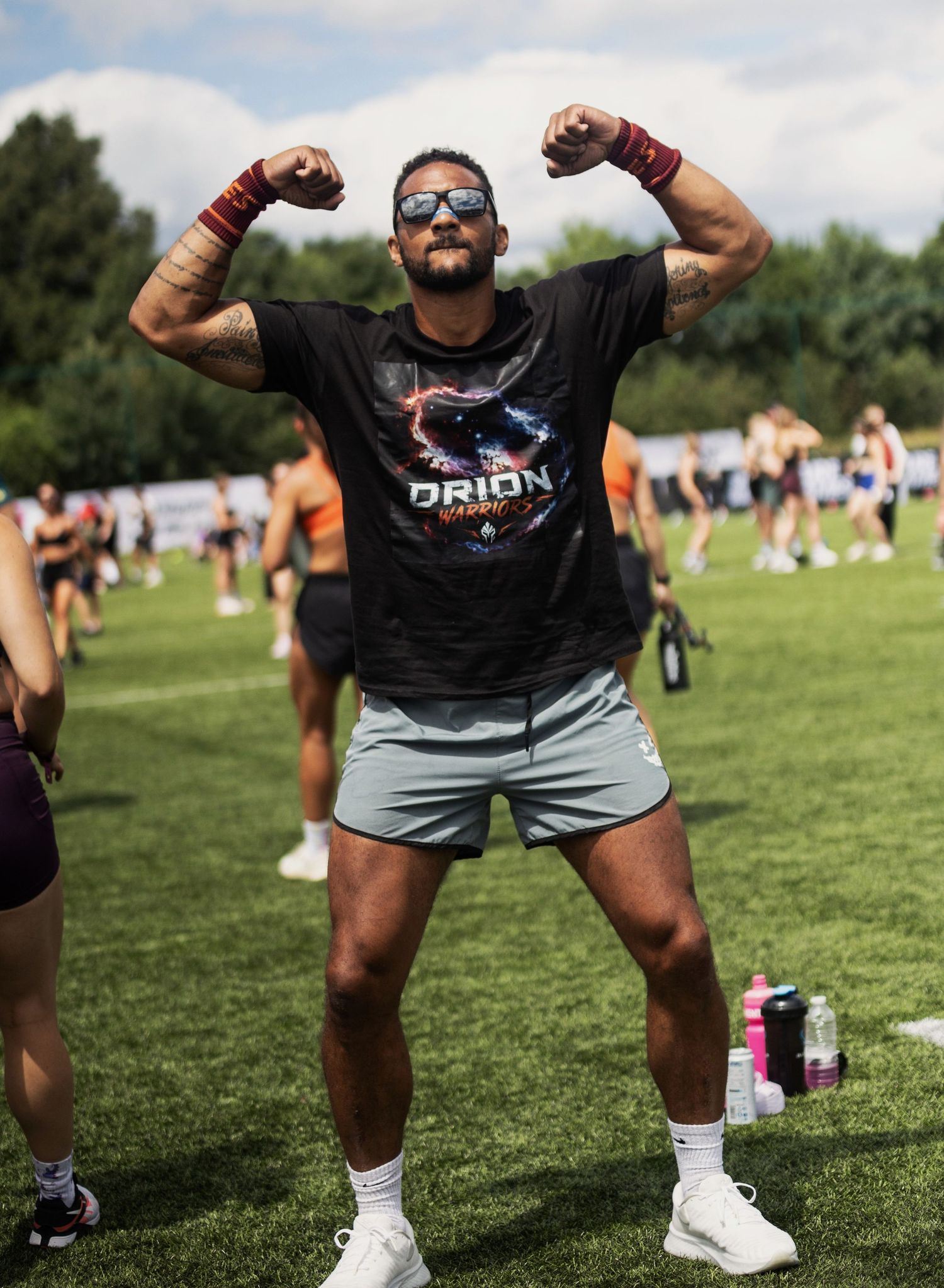 Sports Event Photography - Muscular man in Orion shirt flexing both arms at an outdoor CrossFit competition.