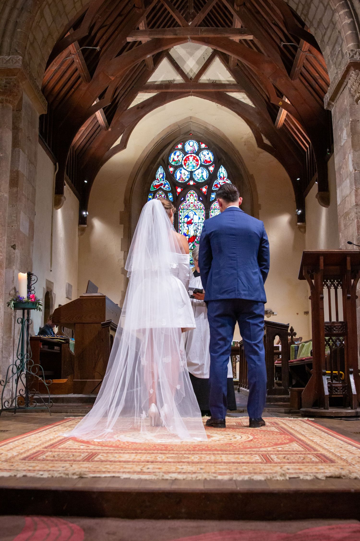 Bride and groom standing at the altar of a historic church with stunning stained glass window.