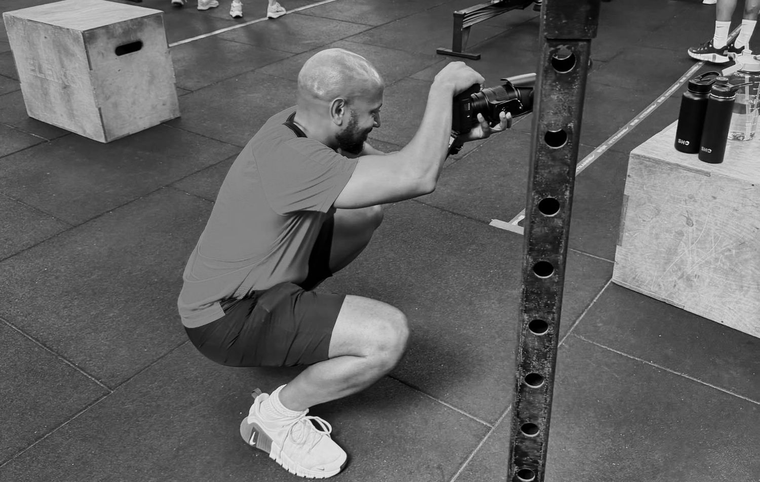 Black and white photo of a man crouching to adjust equipment on a barbell in a gym.