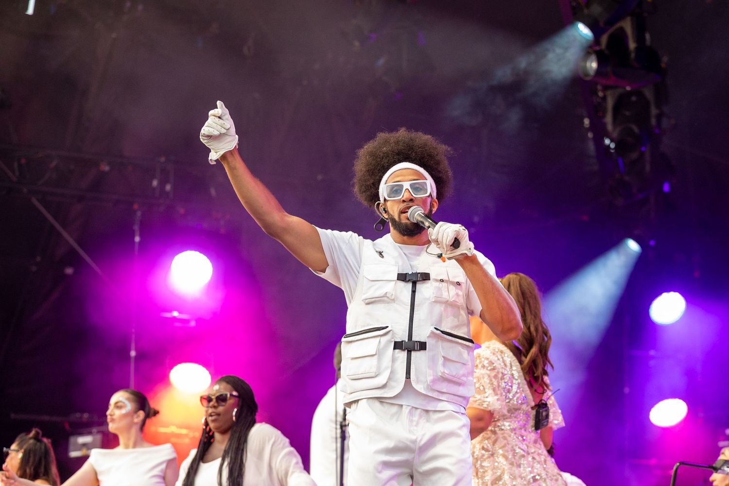 Live Music Event Photography - Male performer in white outfit with afro hairstyle singing on stage at an outdoor music festival.