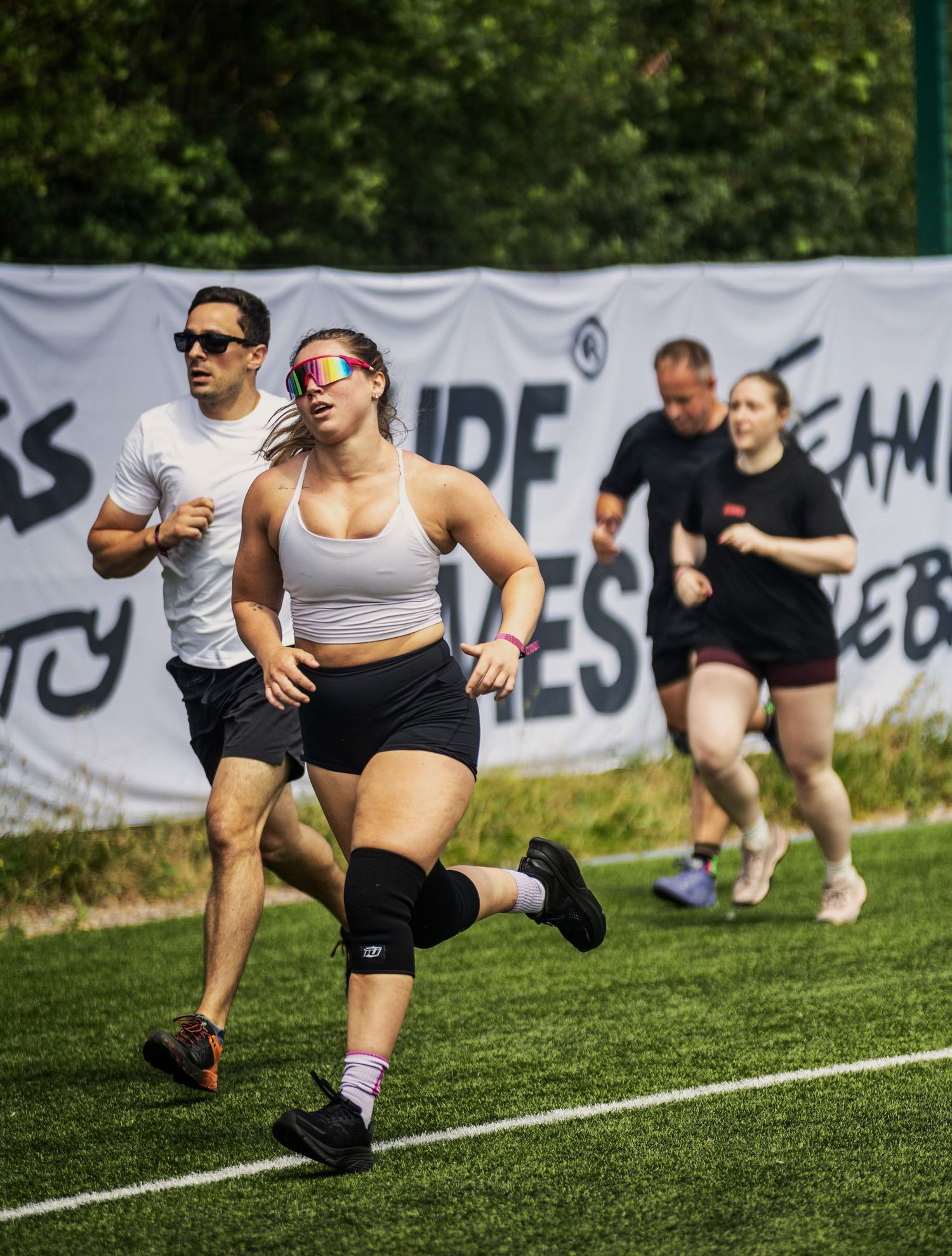 Sports Event Photography - Woman in white sports bra and colorful sunglasses running on grass at an outdoor fitness competition.