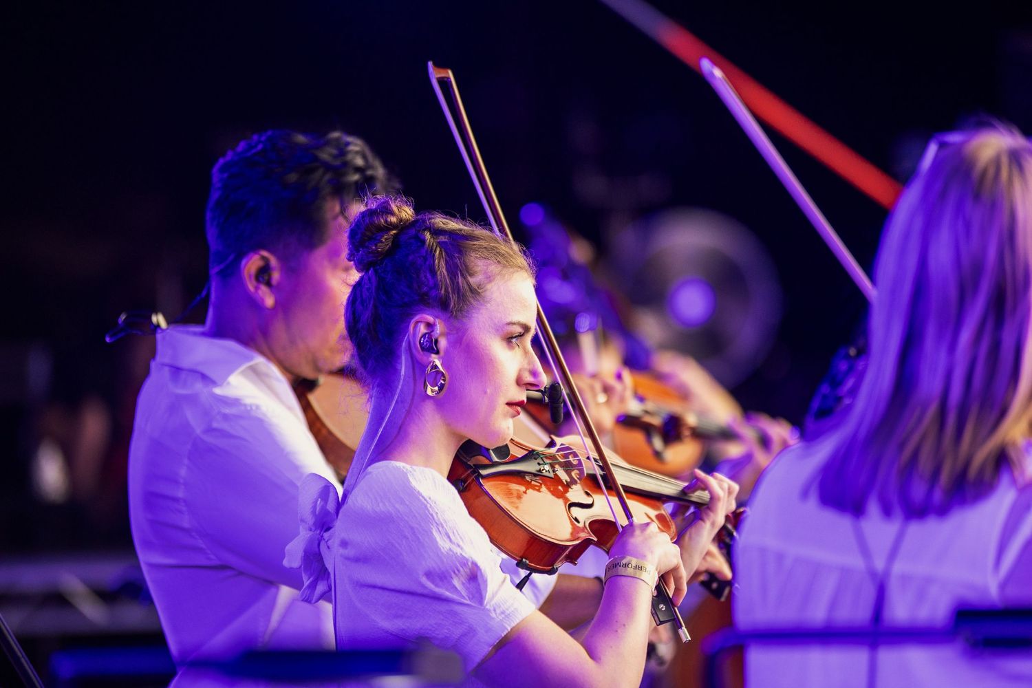 Live Music Event Photography - Young violinists performing in an orchestra at a live concert under blue stage lighting.
