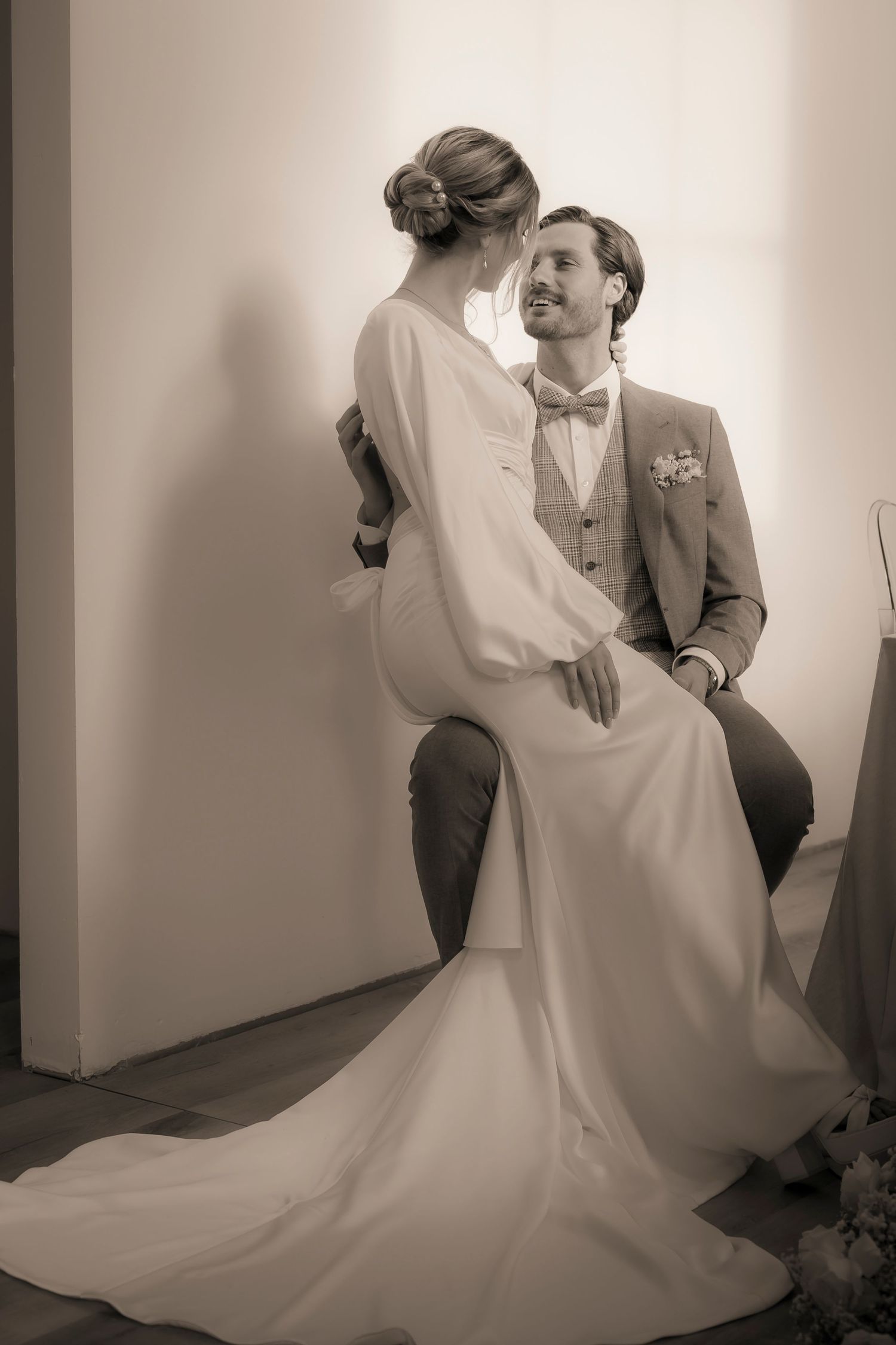 Sepiafarbenes Hochzeitsfoto der Braut im weißen Kleid und des Bräutigams im grauen Anzug mit Fliege, die einen intimen Moment teilen.