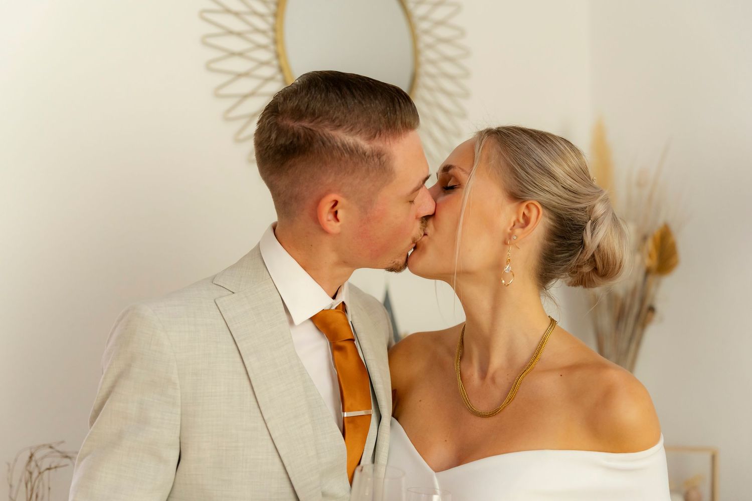 Braut und Bräutigam tauschen einen romantischen Kuss in eleganter Hochzeitskleidung aus, im Hintergrund ein Spiegel im Boho-Stil.