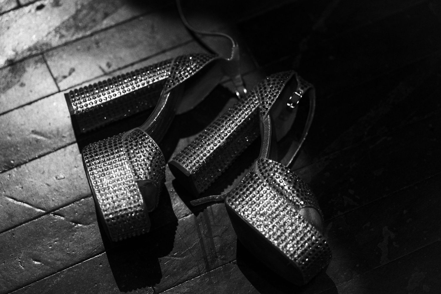 Close-up black and white shot of sparkly high heels laying on floor.