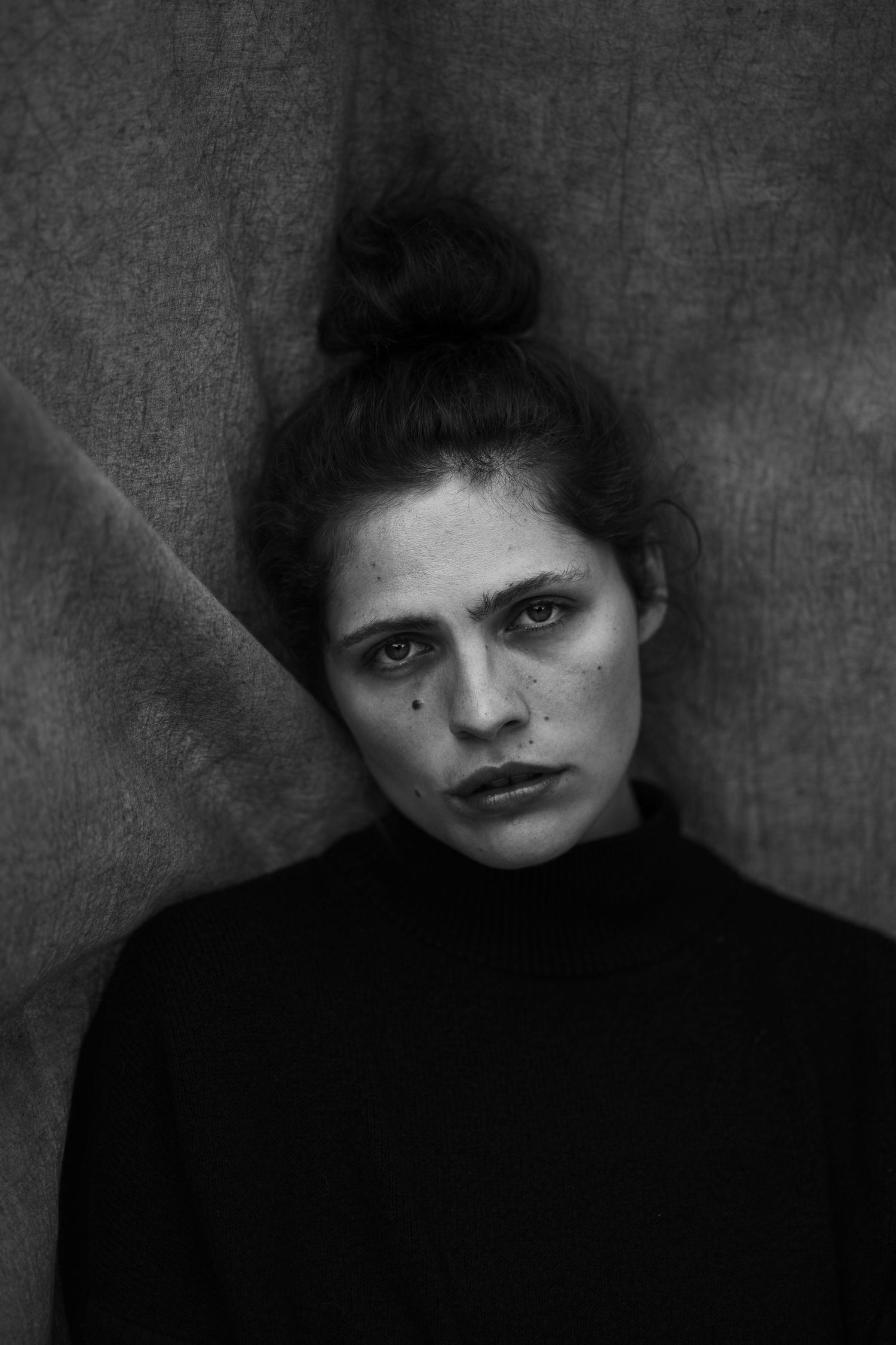 Moody black and white portrait with turtleneck sweater against textured background.