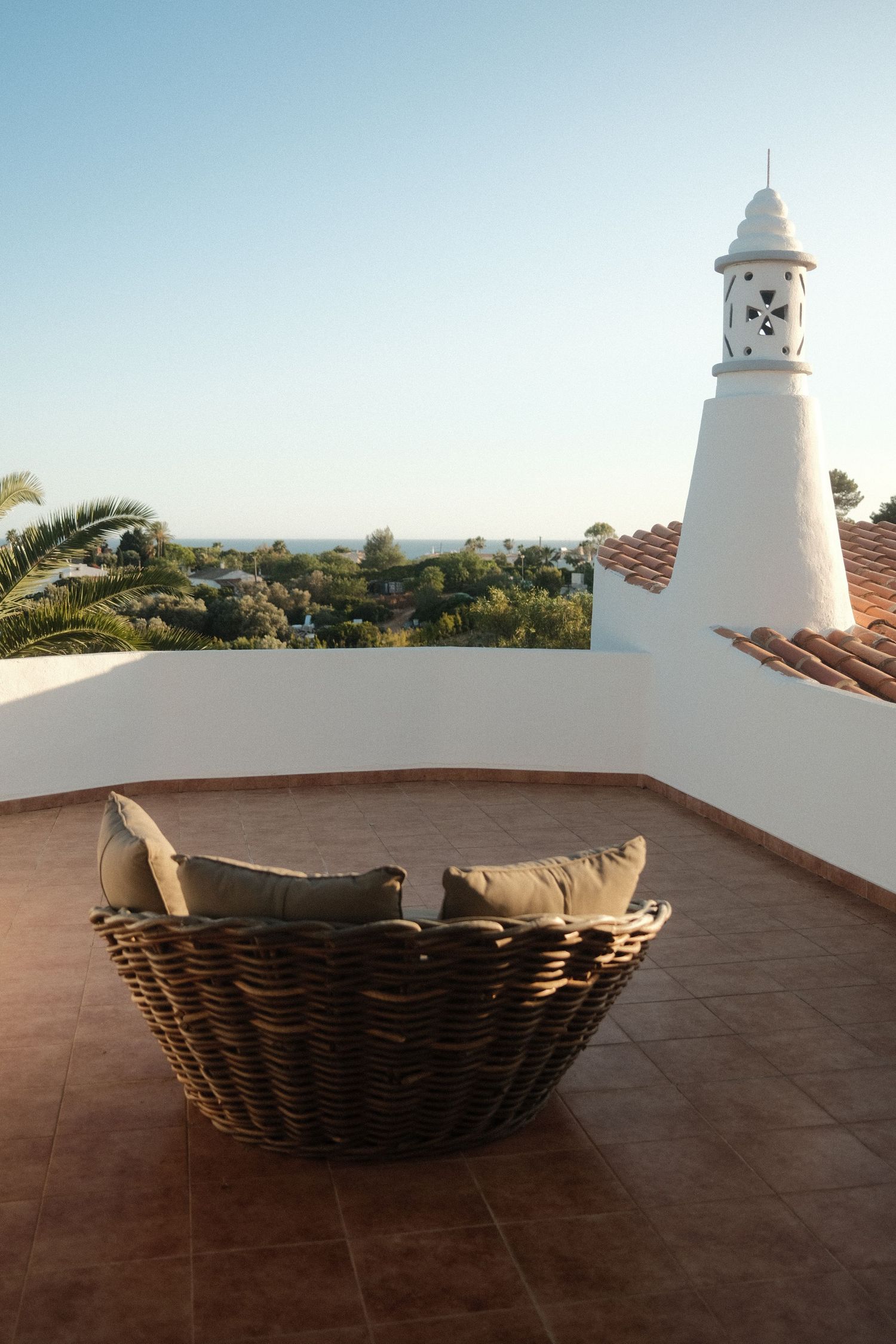 Mediterranean terrace with wicker basket seating and white bell tower against blue sky.
