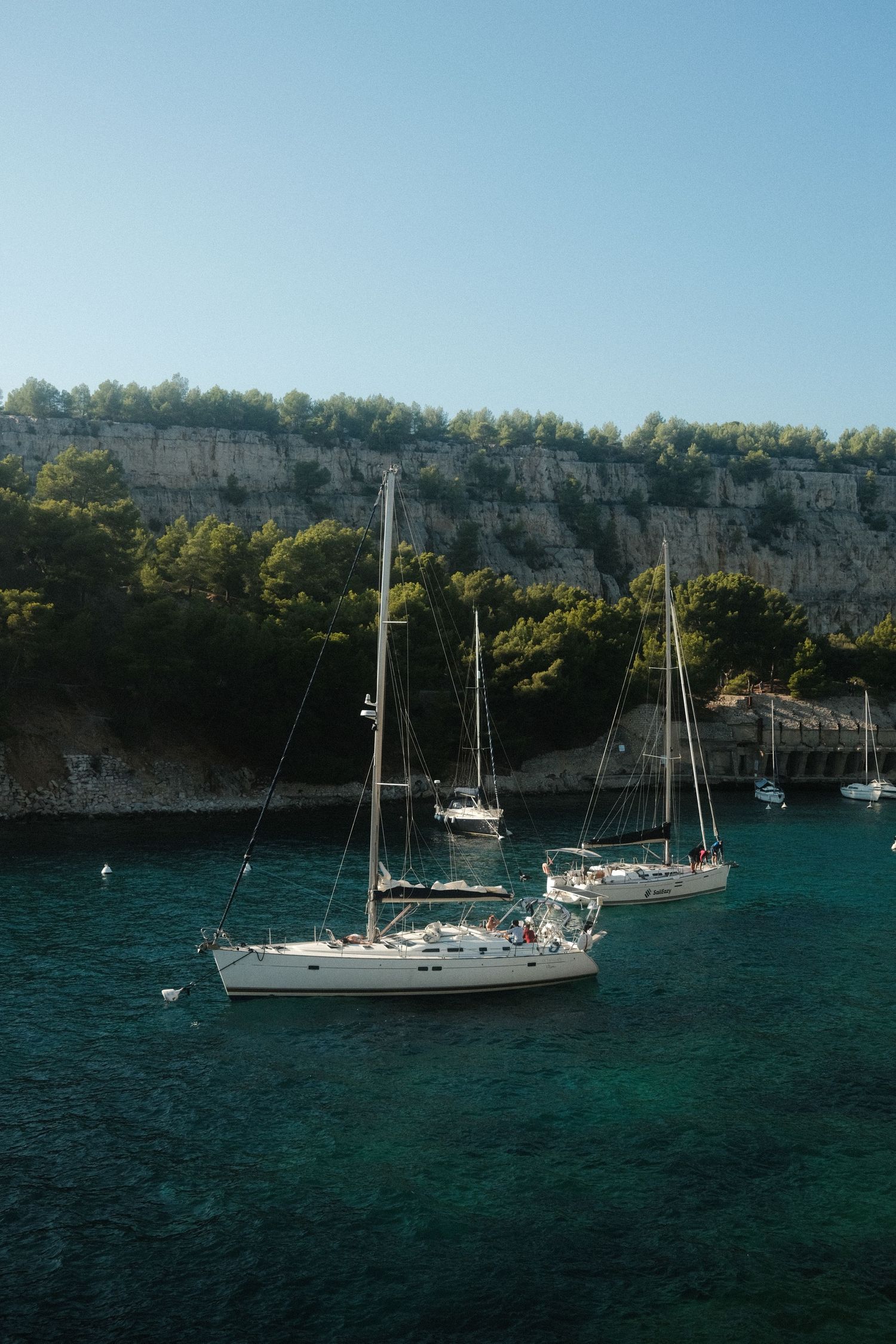 Several sailboats anchored in turquoise waters near dramatic limestone cliffs.