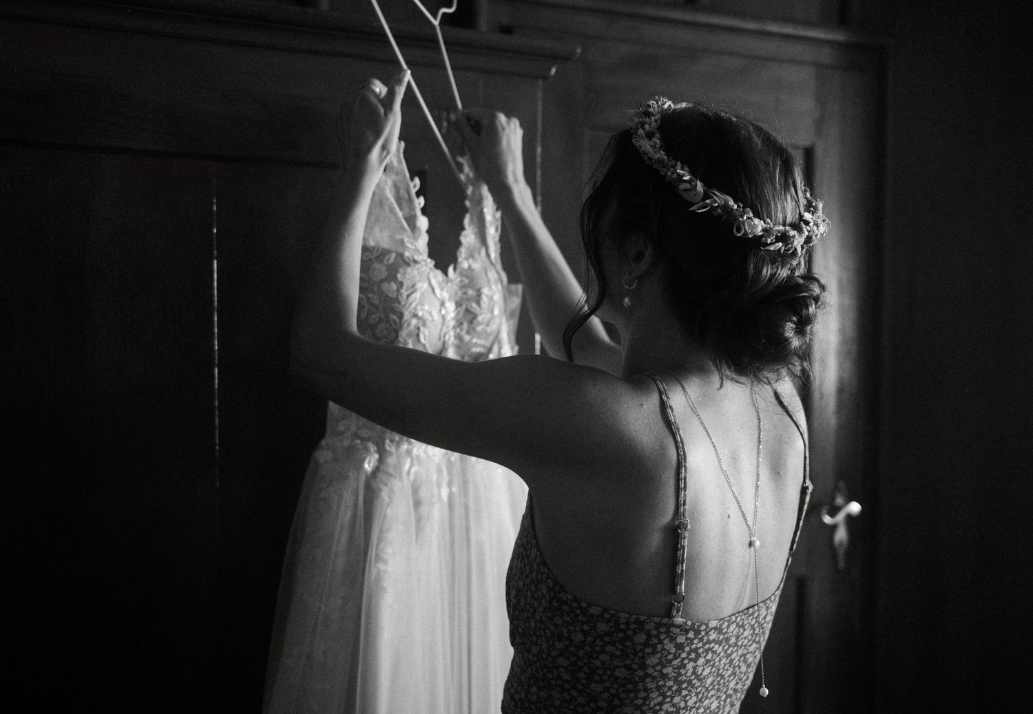 Elegant wedding dress hangs in a dark room with soft lighting creating a dramatic silhouette.