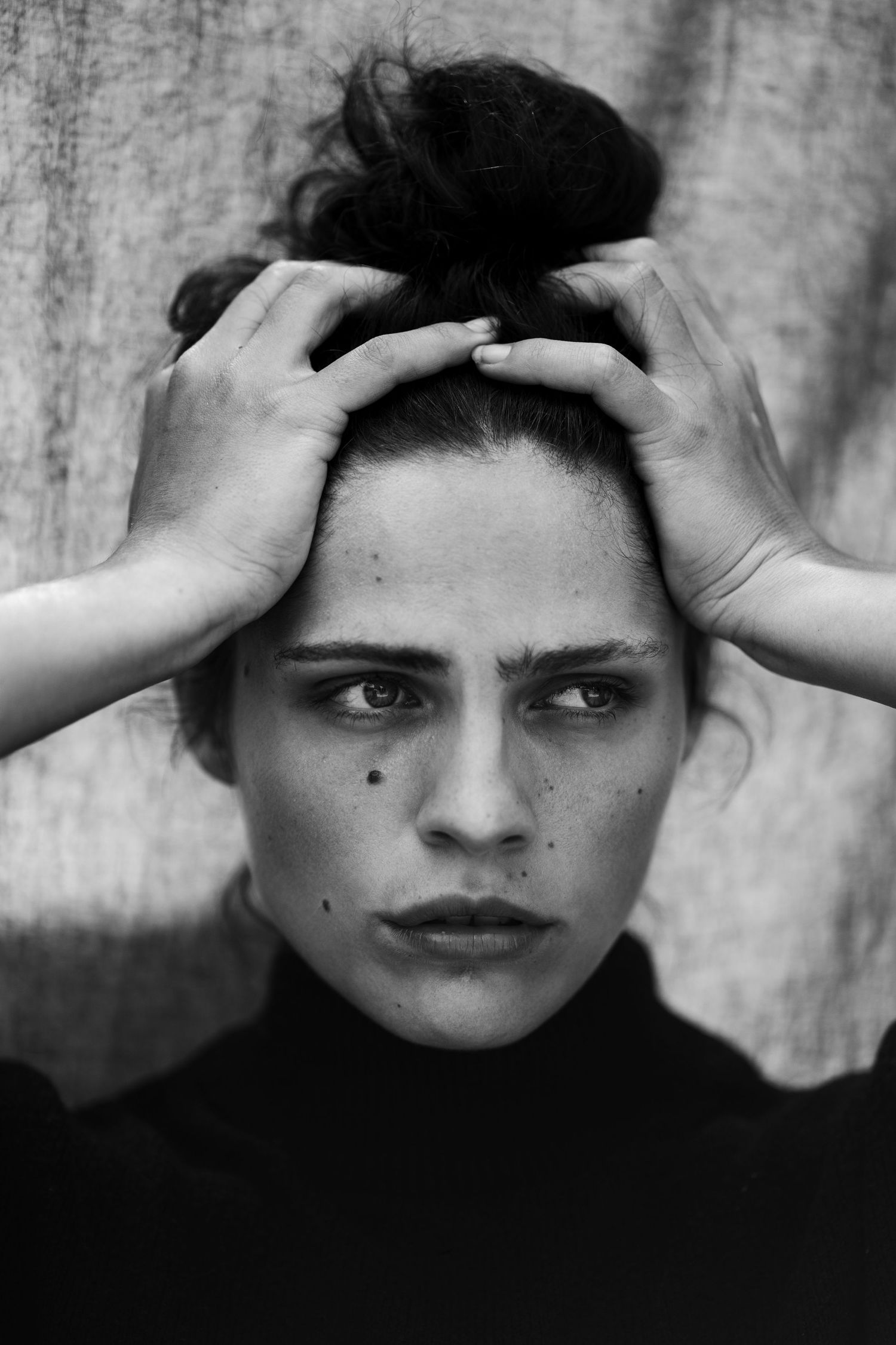 Expressive black and white portrait with hands positioned near the head against a textured wall.