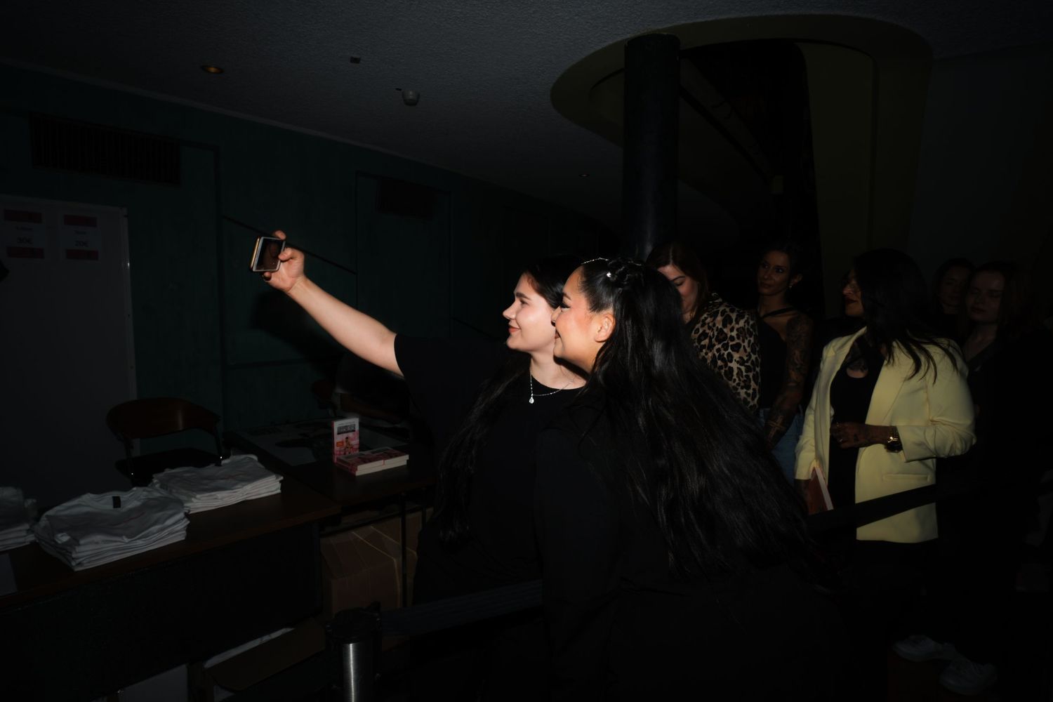 Concert venue backstage scene with Bahar Kizil taking selfie with a fan in dark lighting.