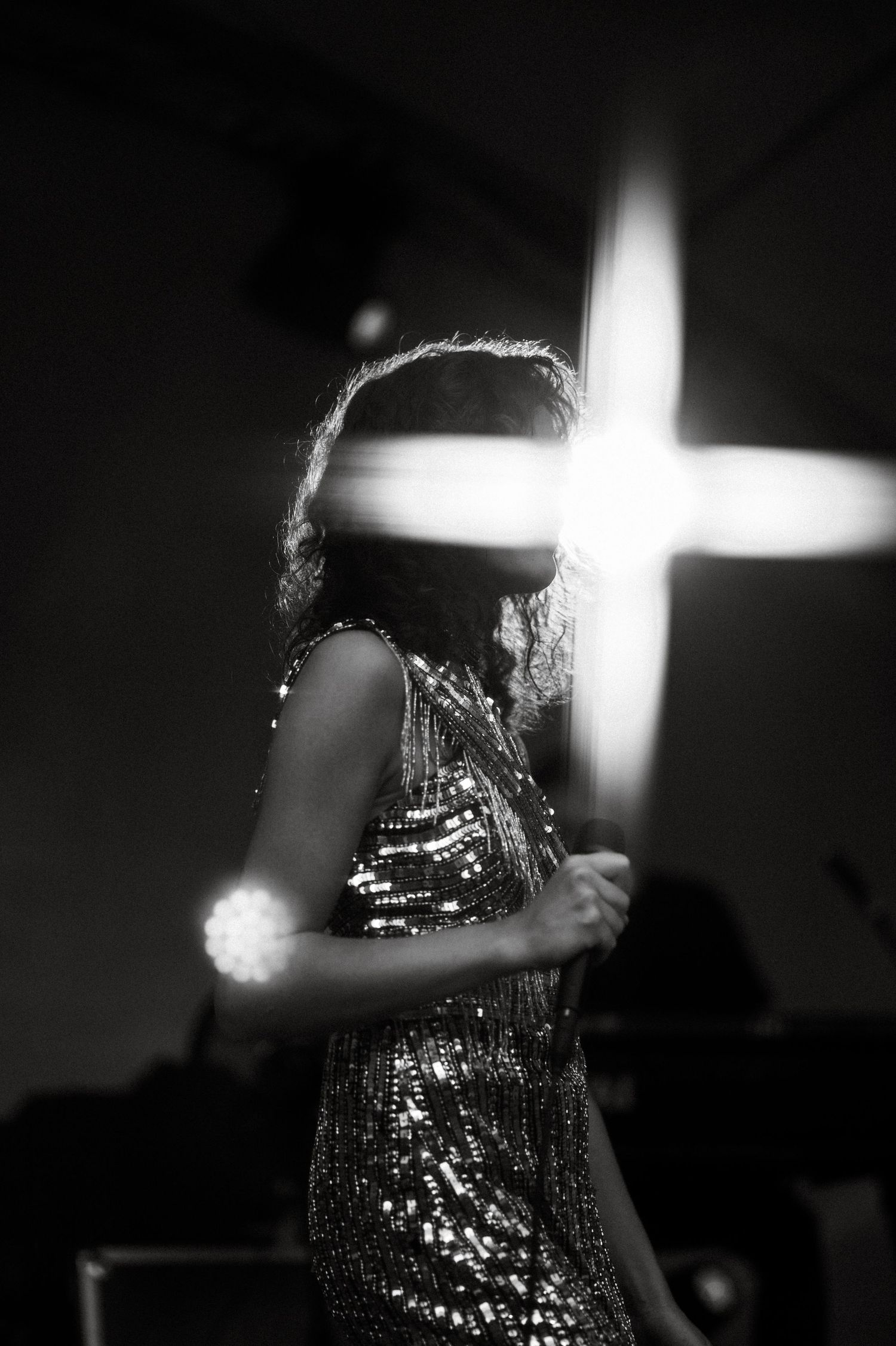 Silhouetted figure in sparkly dress with illuminated cross in background.