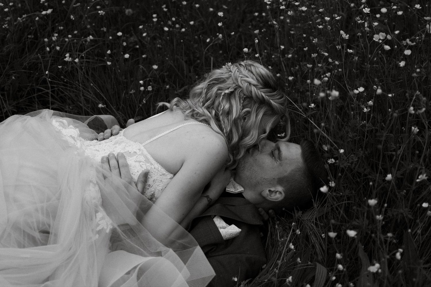 Romantic black and white photo of wedding couple resting in a flower-filled meadow.