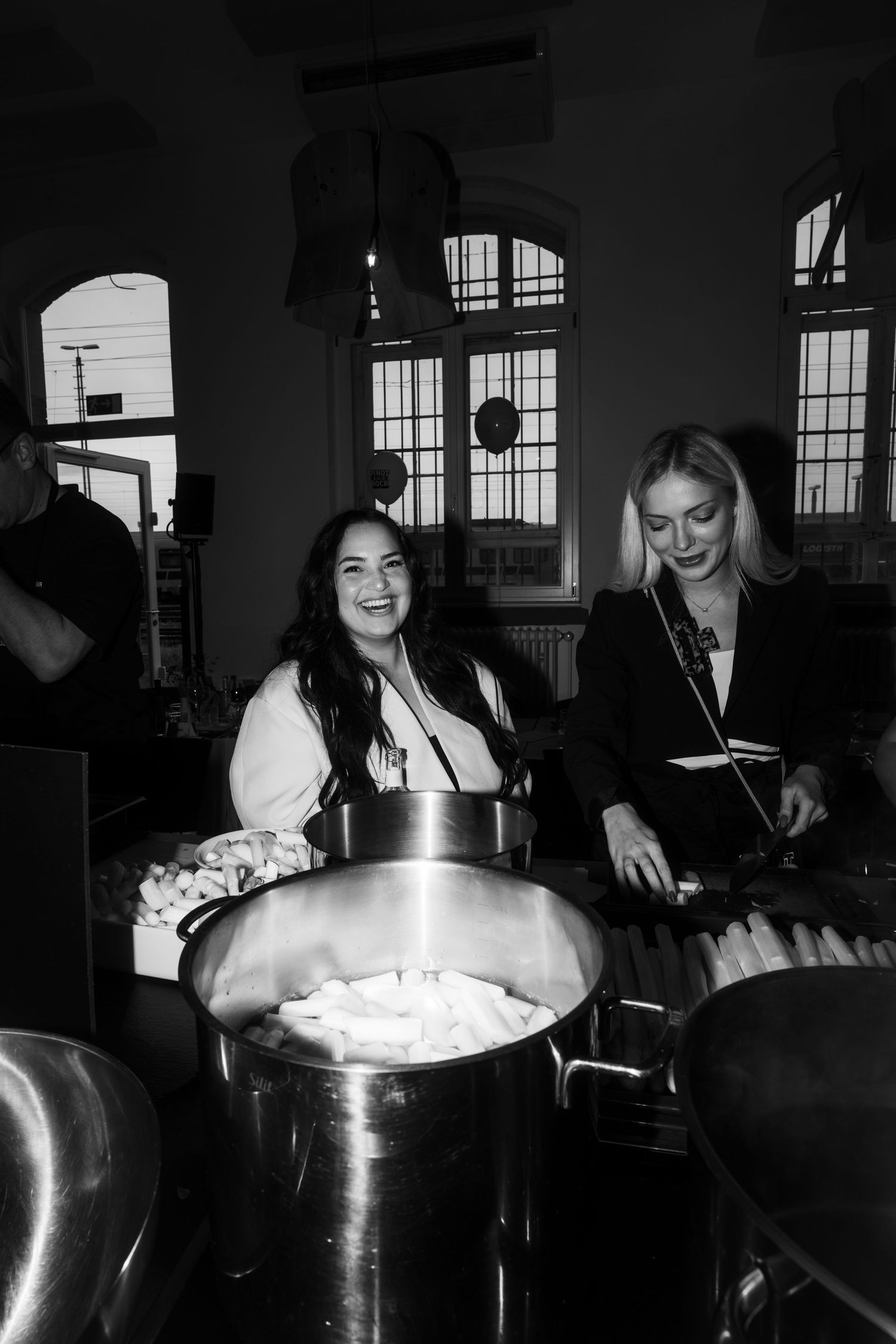 Group of people gathered around large steaming pots in a dimly lit indoor setting.