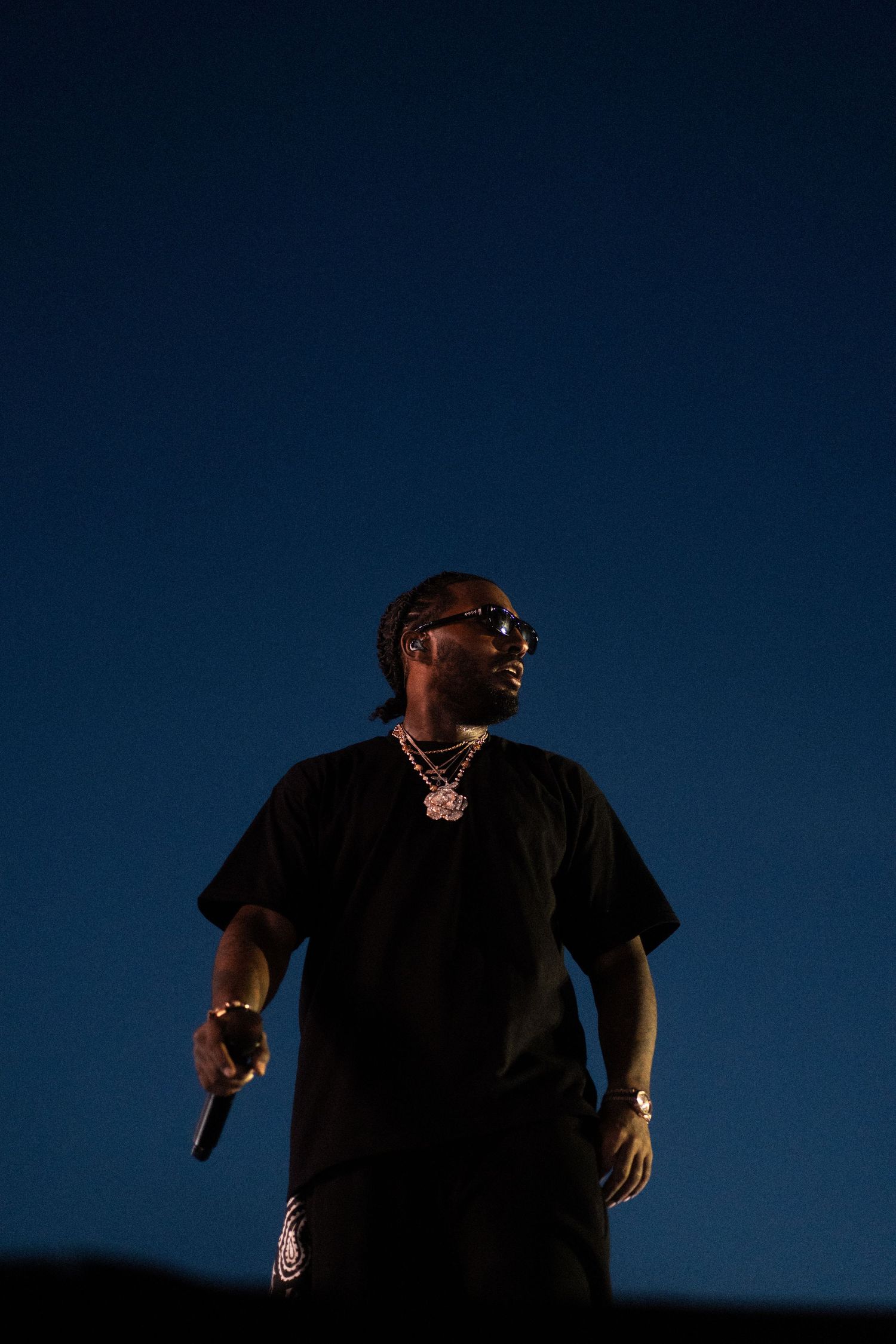 Reezy silhouetted against deep blue evening sky on outdoor stage.
