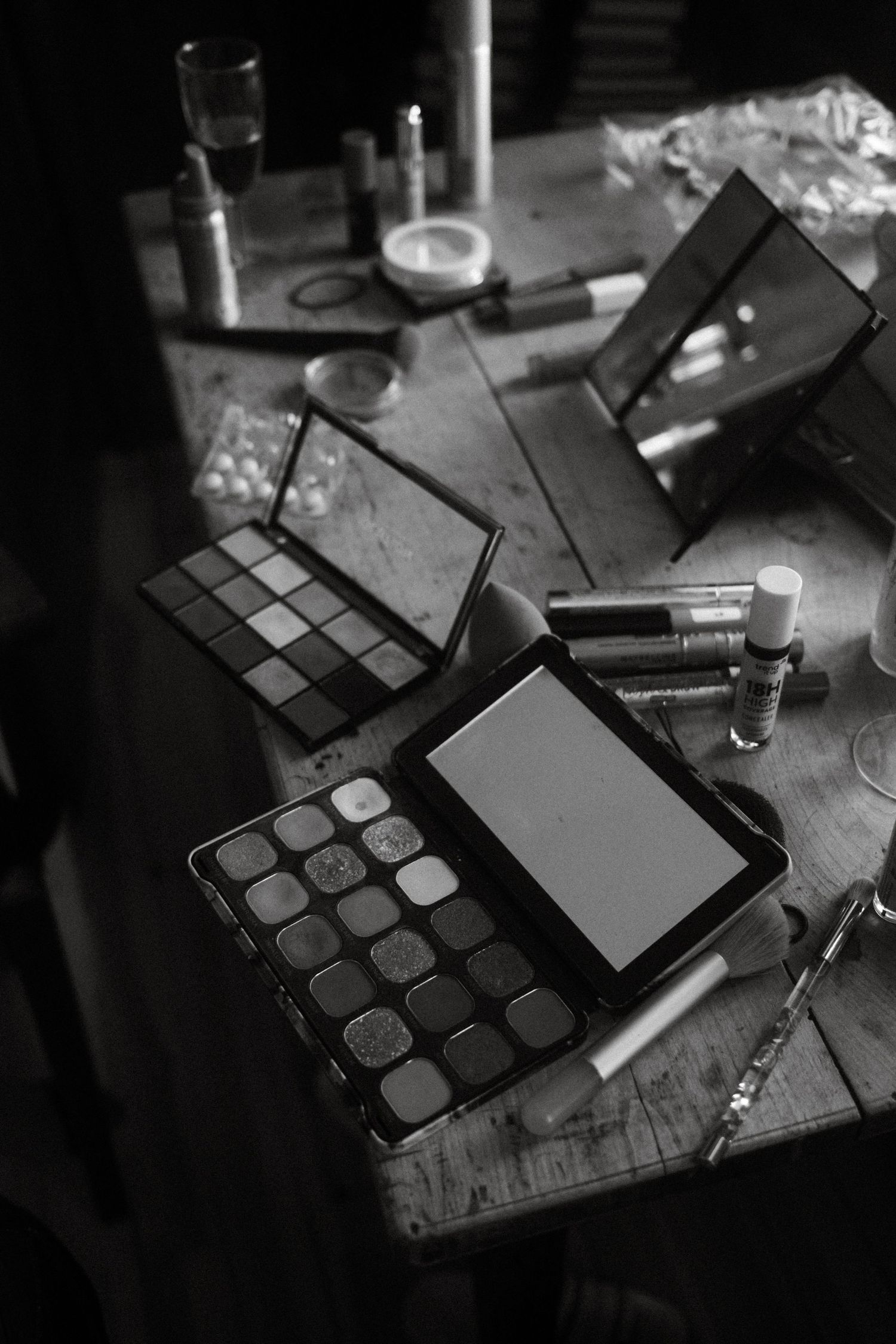 A makeup palette and beauty products arranged on a wooden surface in black and white.