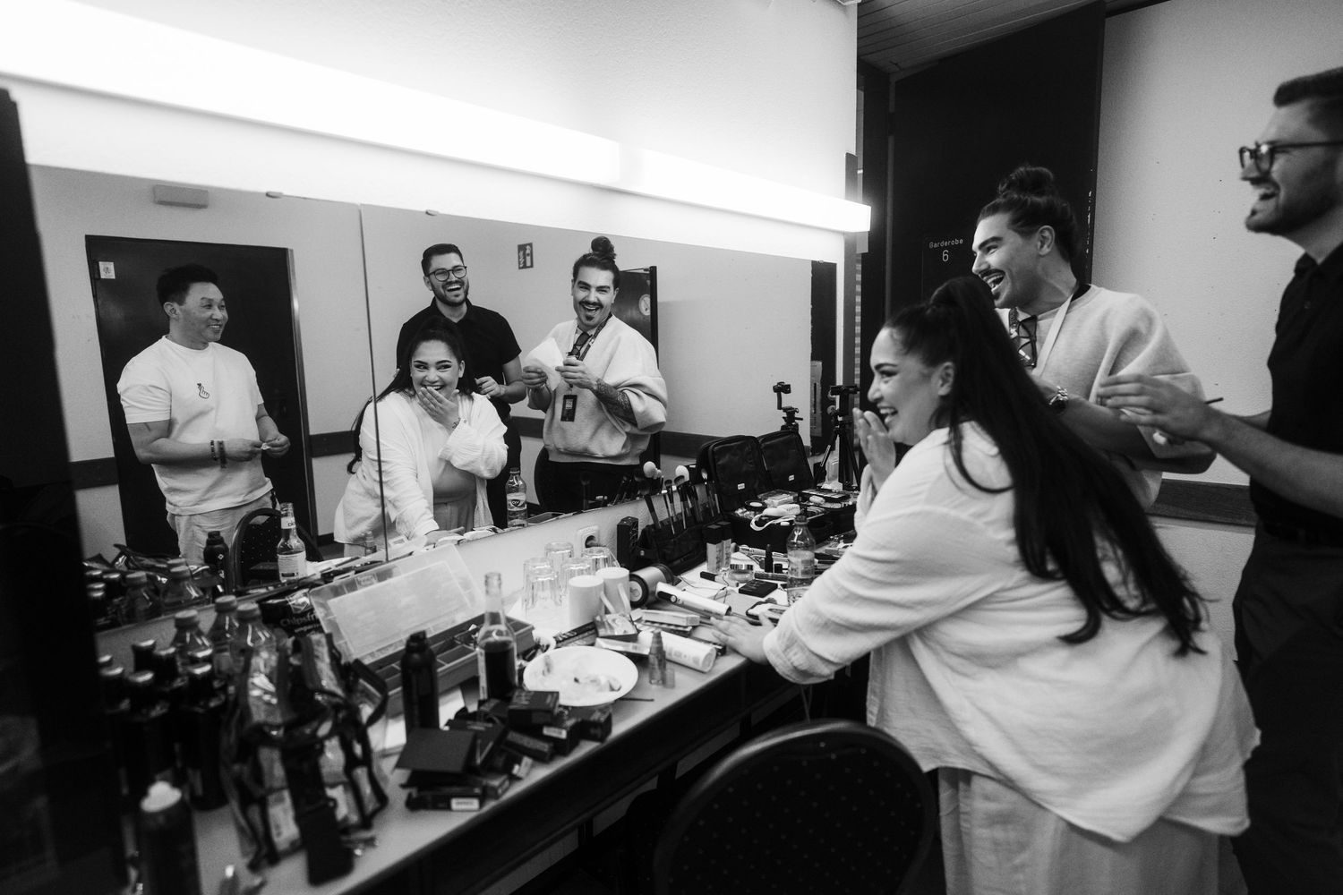 Behind-the-scenes preparation scene with multiple people in a bright indoor setting.