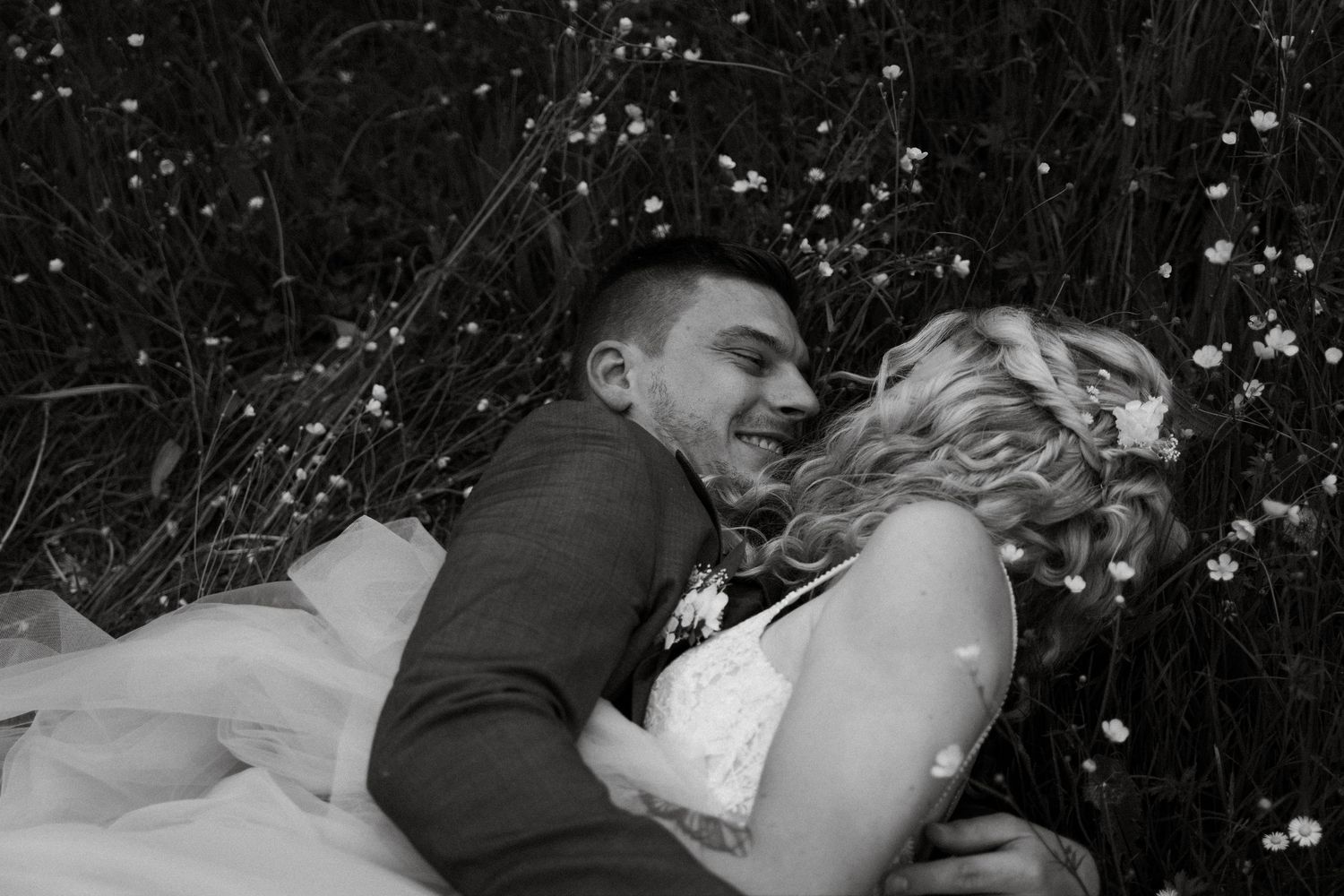 Black and white intimate moment between newlyweds lying in a flower field.