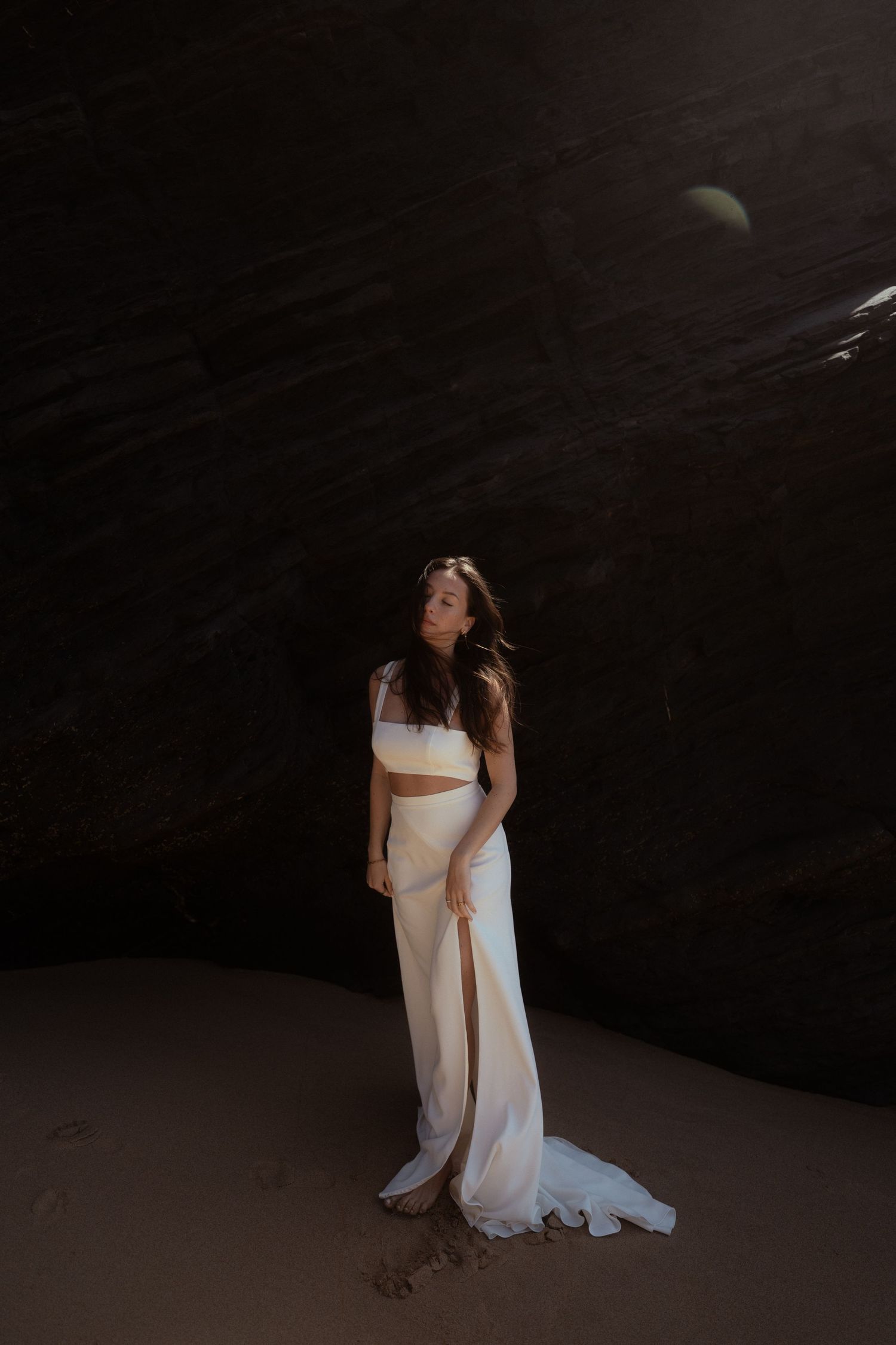 Ethereal bridal portrait in a flowing white two-piece dress against a dark backdrop with moon.