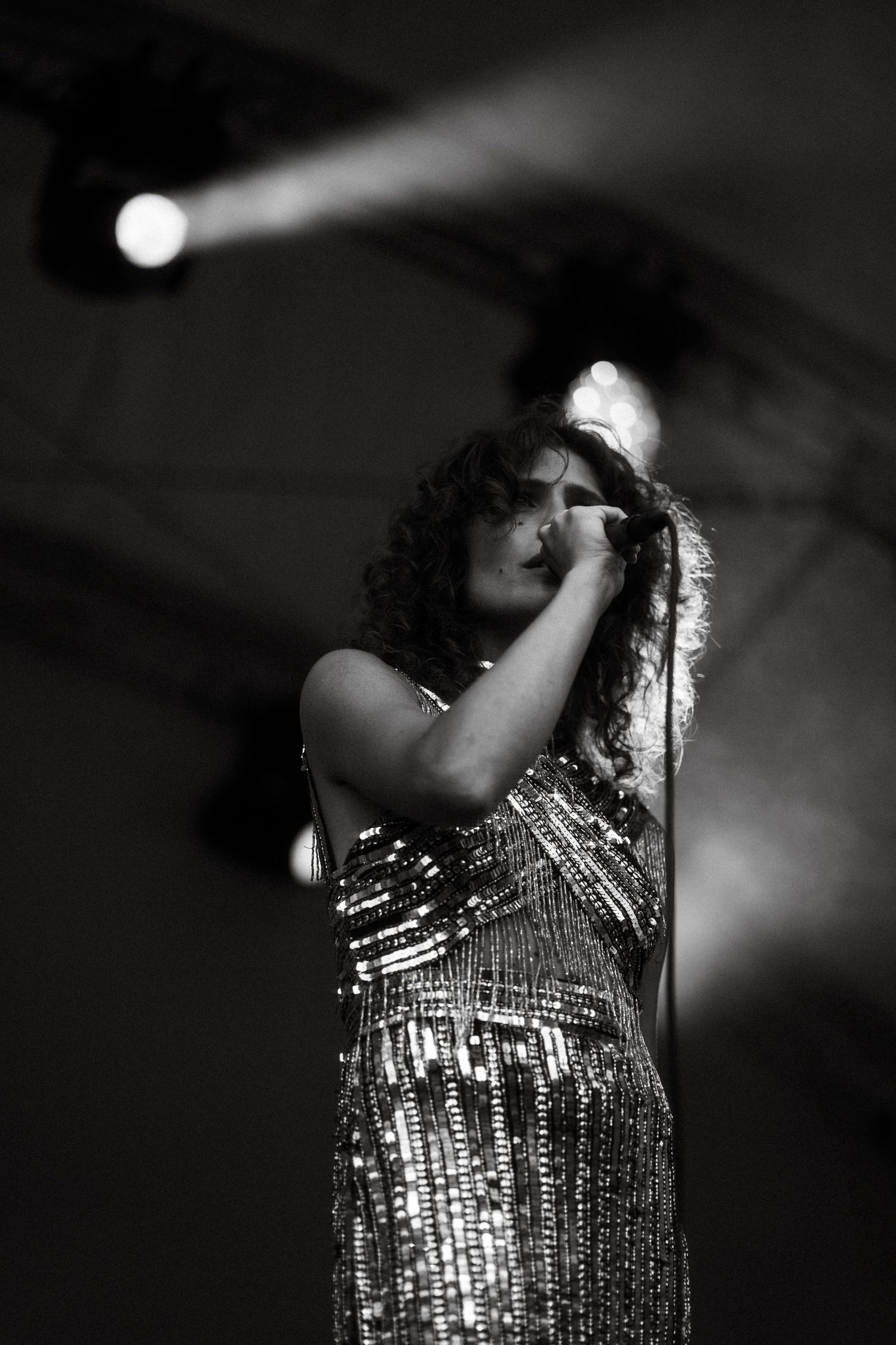 Performer in a sparkly sequined dress singing on stage in dramatic black and white lighting.