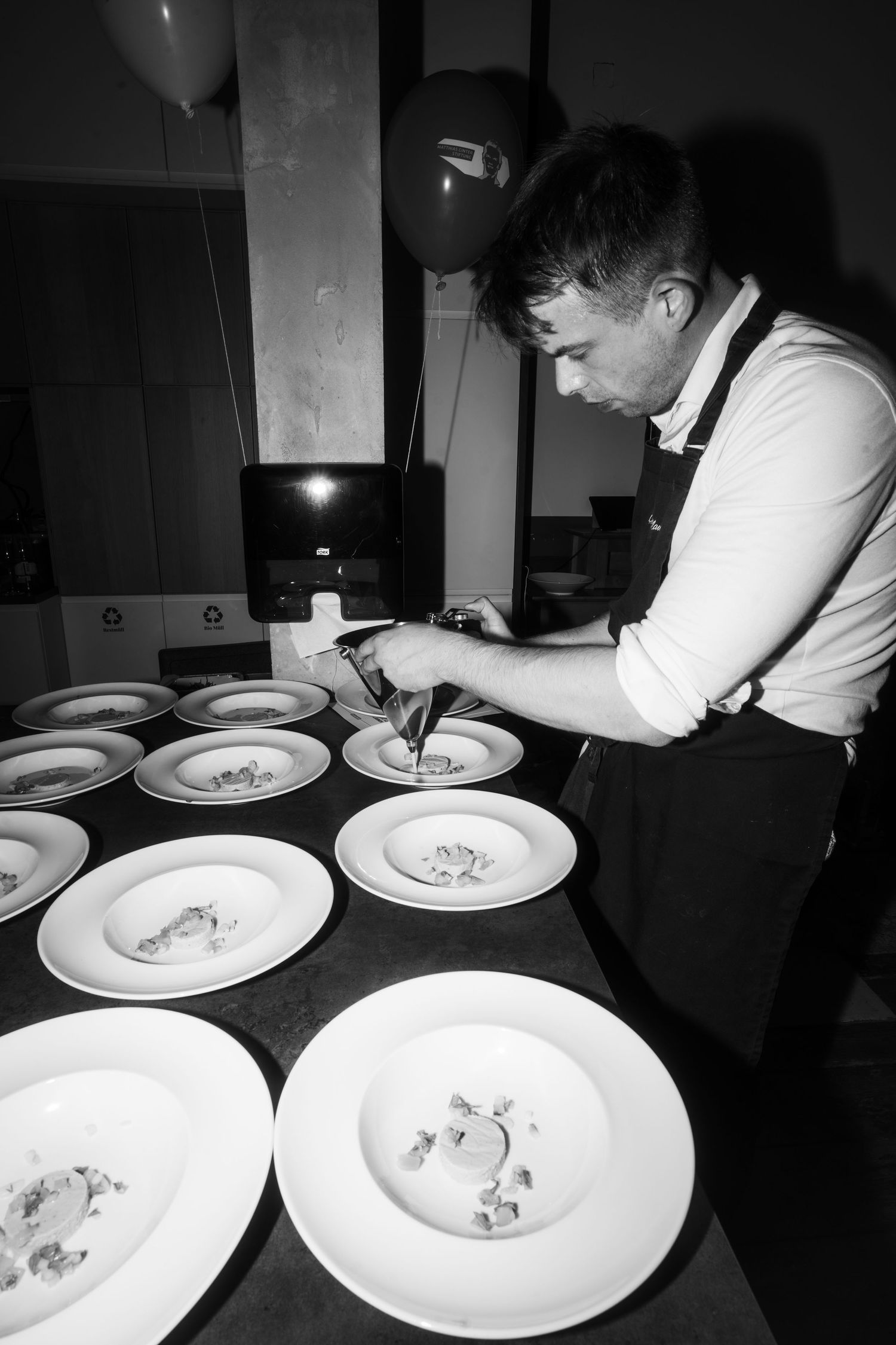 Chef carefully plating and arranging food on multiple white dishes at a preparation station.