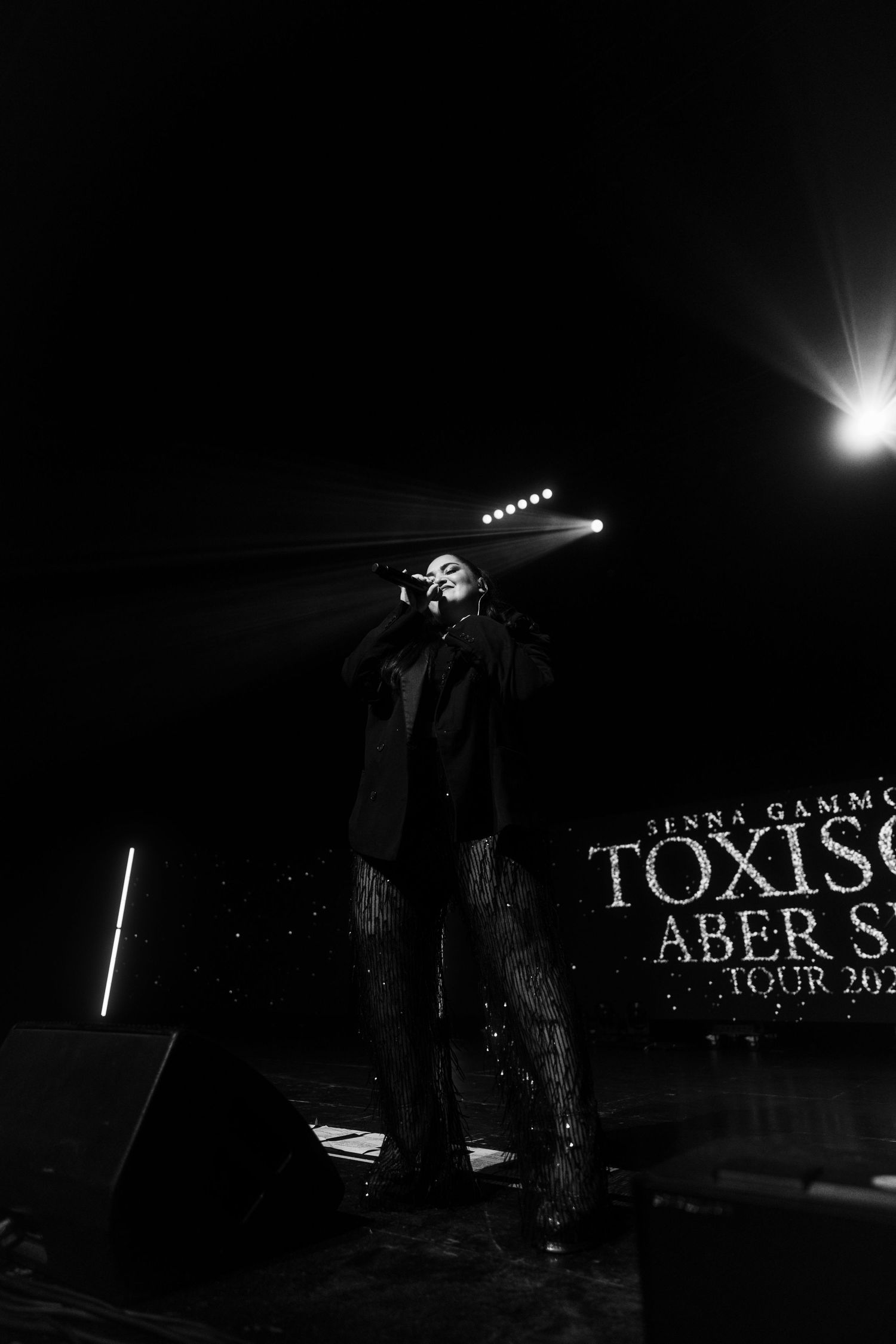 Dramatic black and white concert photo showing silhouette on stage with bright spotlight.