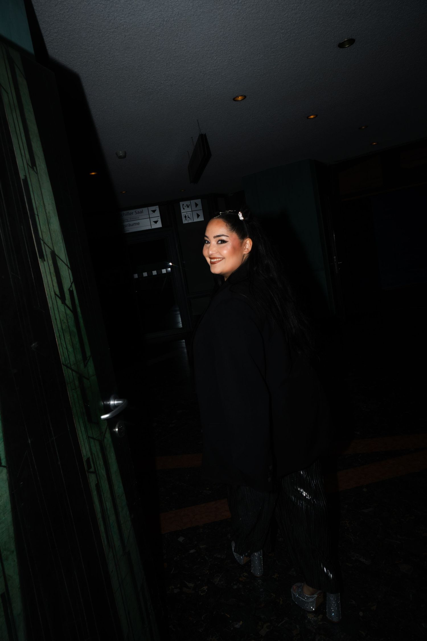 Dark moody photo of Bahar Kizil in all black outfit standing in corridor.