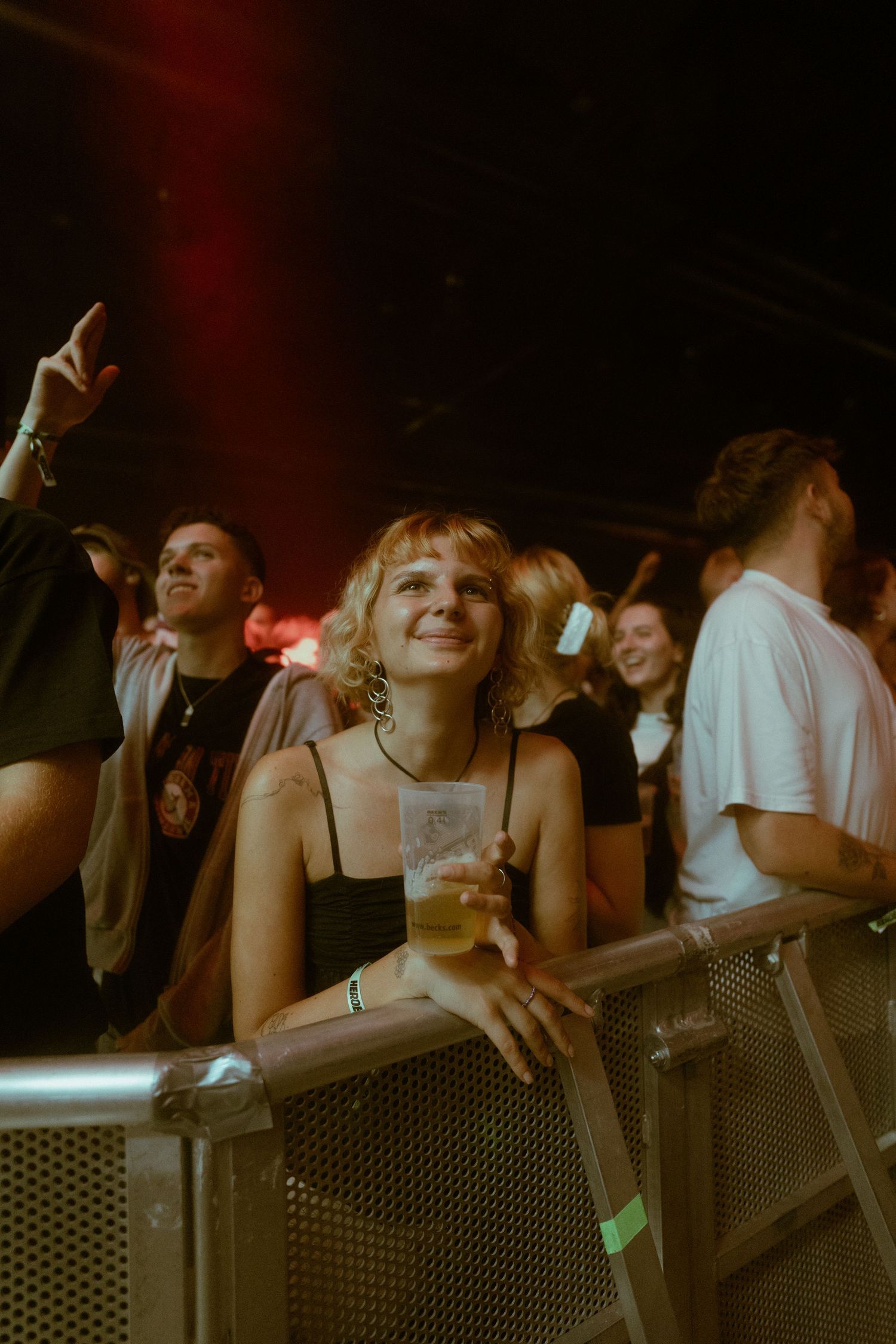 Enthusiastic fans lean against concert barrier in dim lighting.
