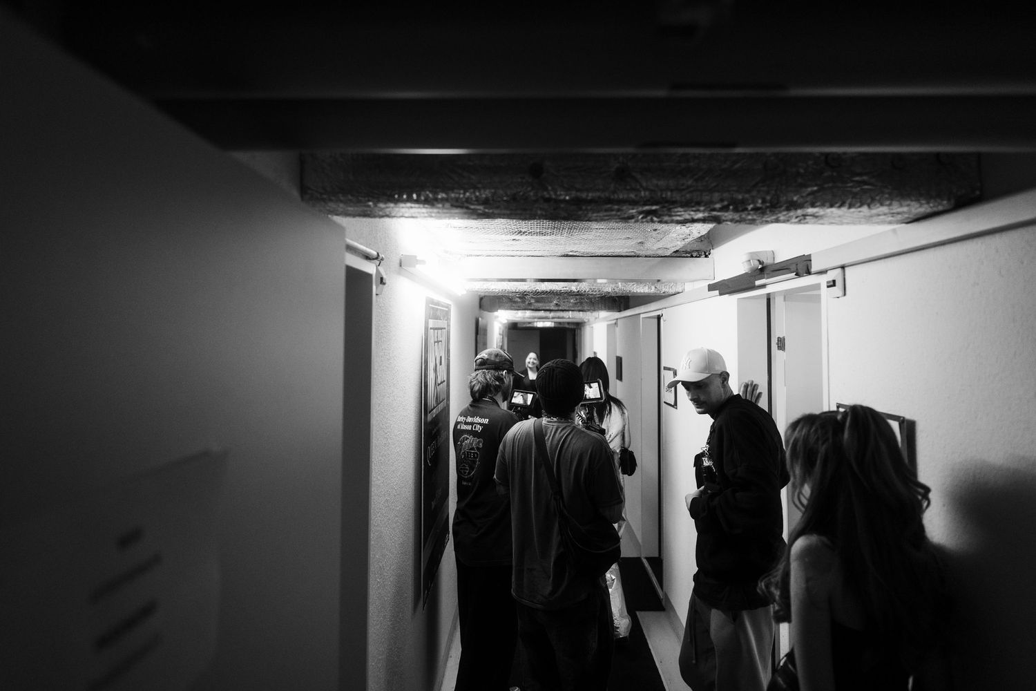 Bahar Kizil and Senna Gammour interact in a narrow hallway with stark lighting and reflective ceiling after show.