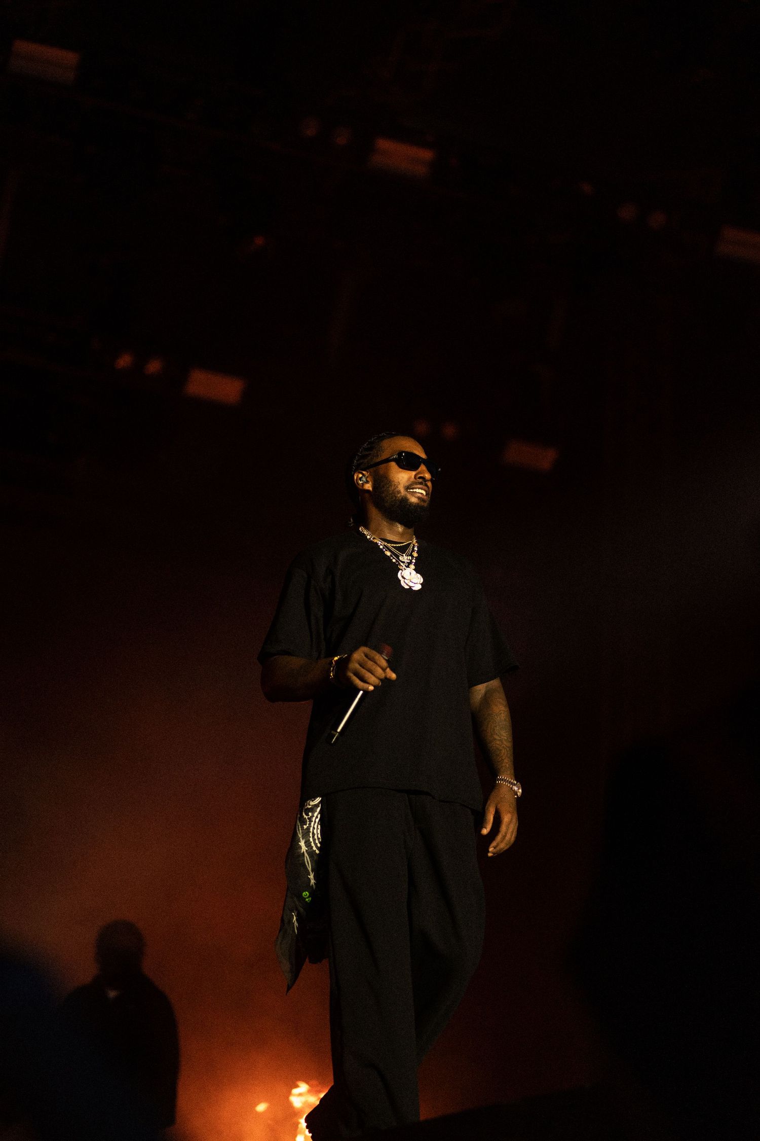 Reezy in dark clothing illuminated by dramatic orange lighting and flames.