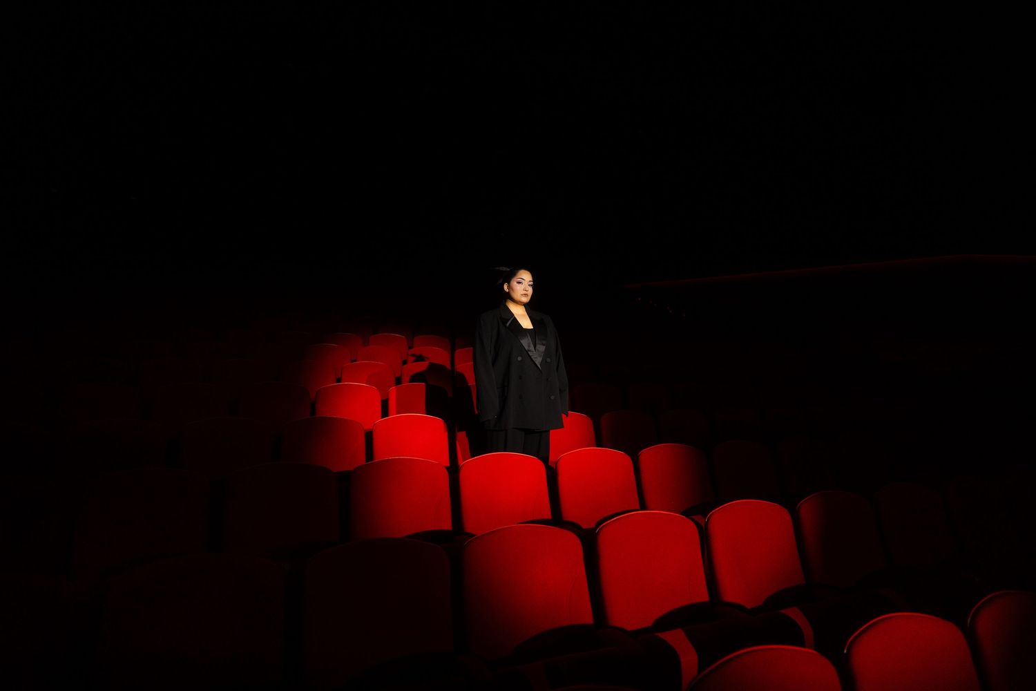 Bahar Kizil seated alone in empty theater with dramatic red lighting on vintage cinema seats, atmospheric cinema ambiance.