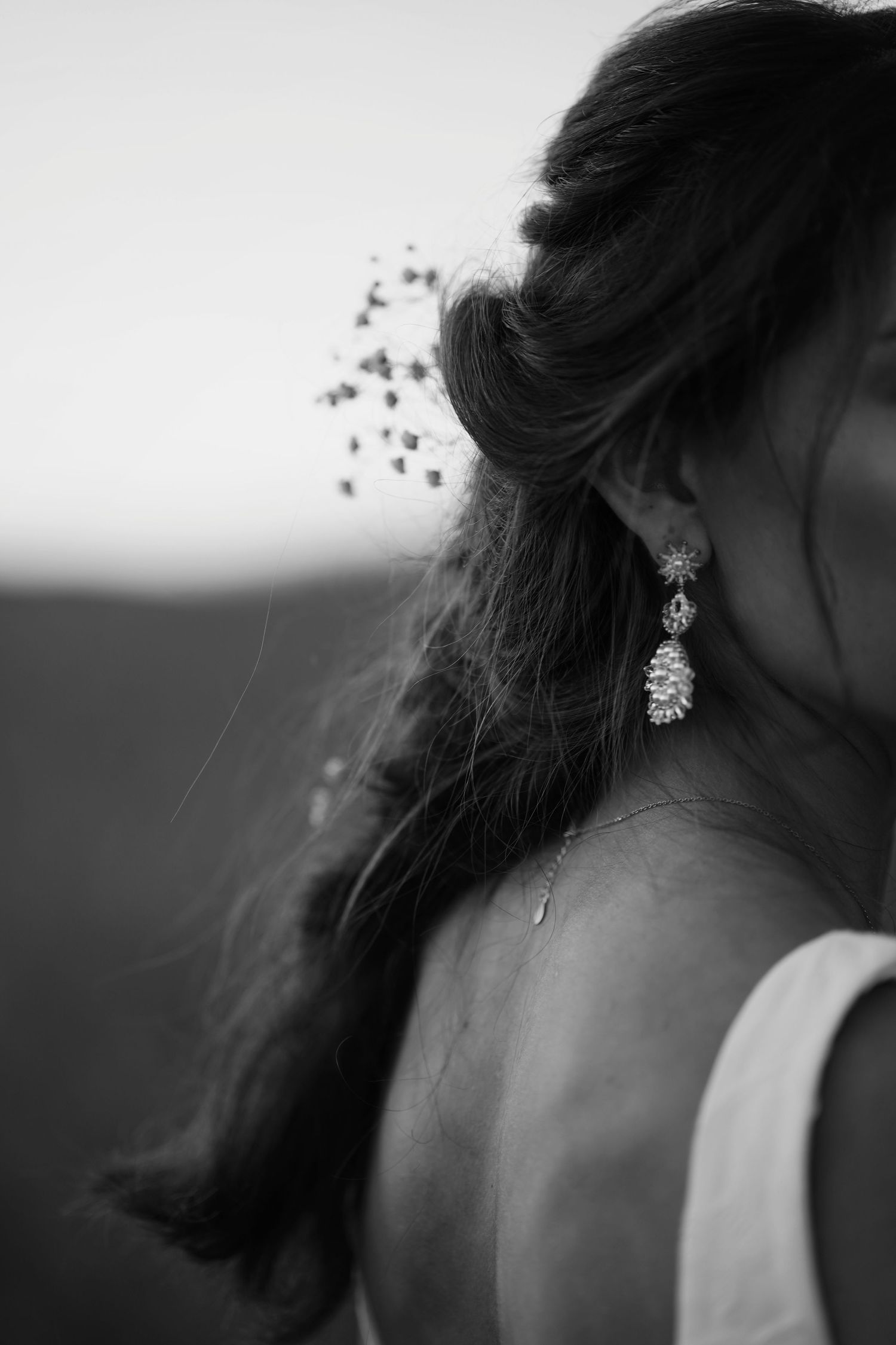 Black and white closeup of delicate crystal earring and bridal hair detail.