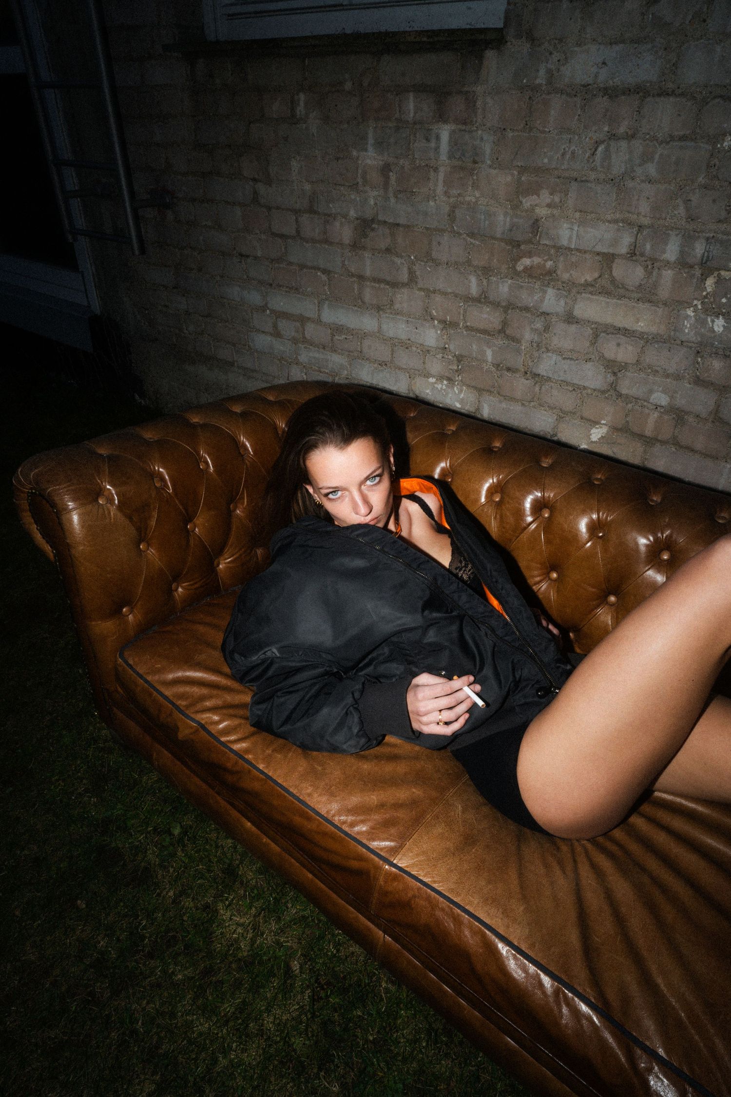 Dramatic photo of a person in dark clothing posed on a brown leather couch.