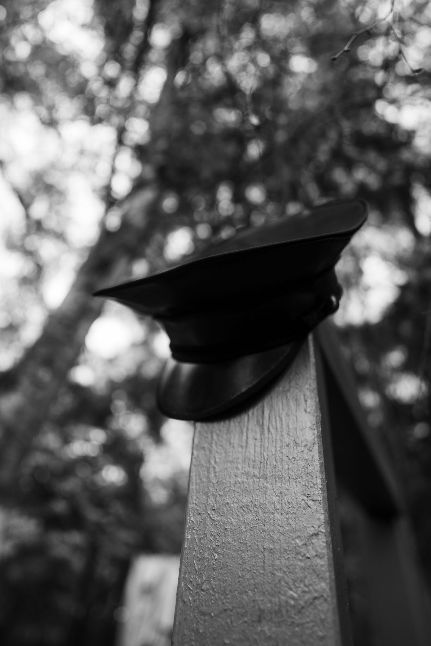 Black military style cap resting on a white wooden post in natural lighting.