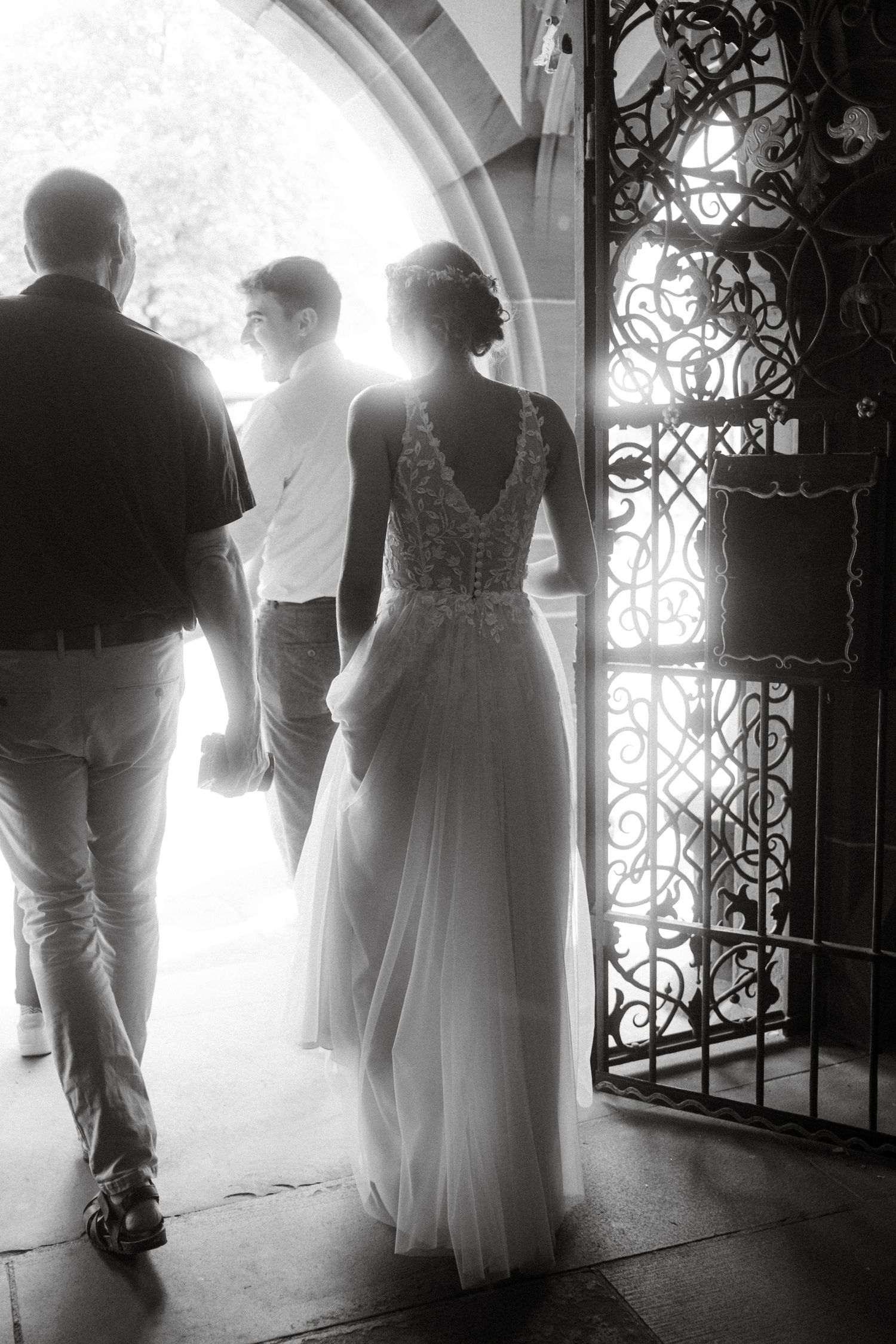 A black and white wedding photo captures silhouettes walking through an ornate archway.