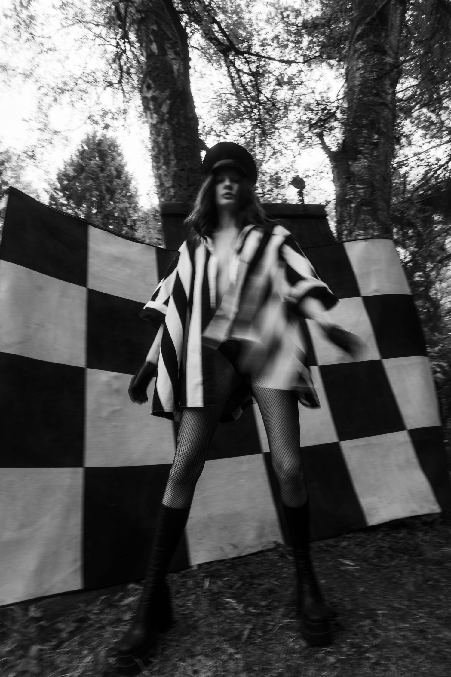 Dynamic low-angle shot of model in striped outfit against checkerboard background.