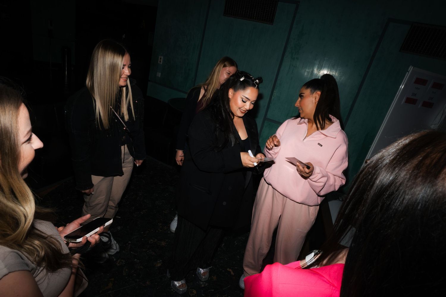 Dimly lit backstage scene with Bahar Kizil, Senna Gammour and fans gathered in casual conversation.