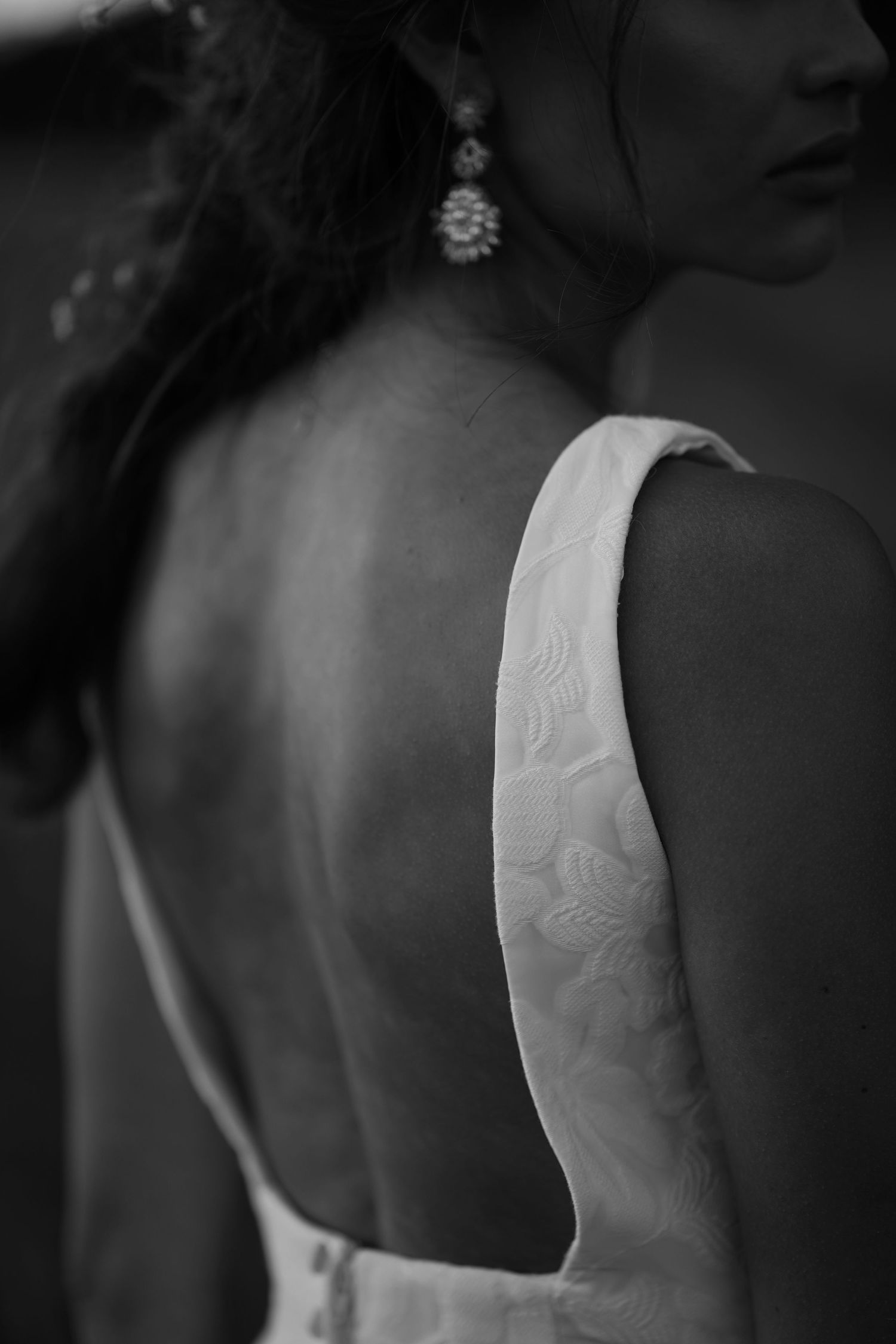 Close-up black and white photo of ornate white wedding dress back detail and earring.
