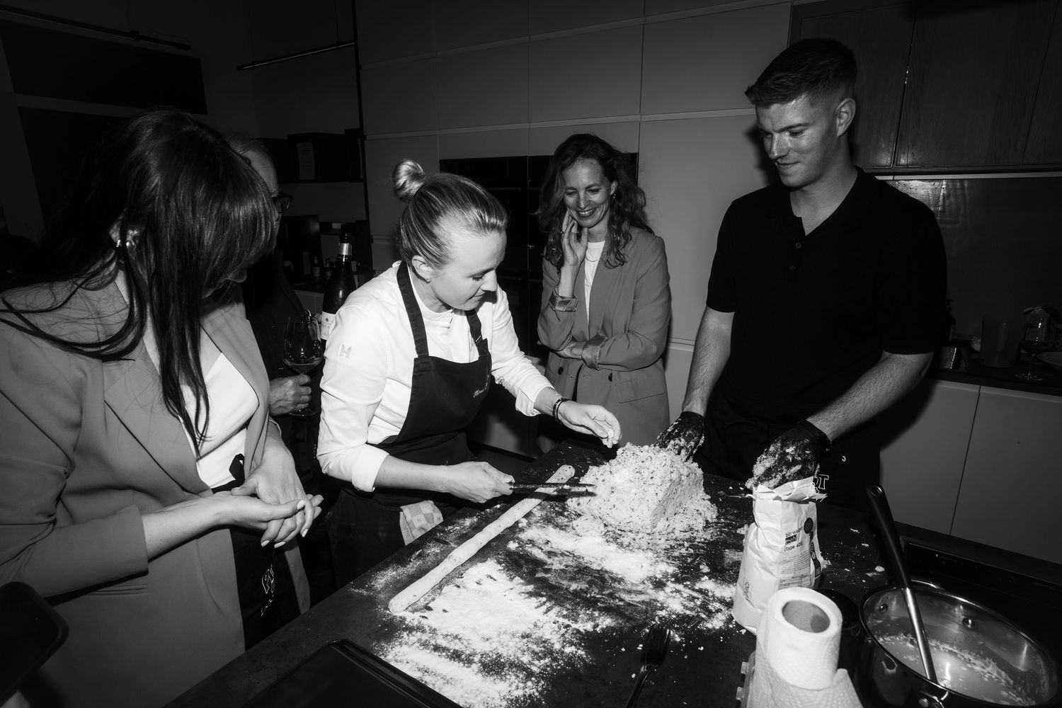 People collaborating in a kitchen while working with ingredients on a flour-covered surface.
