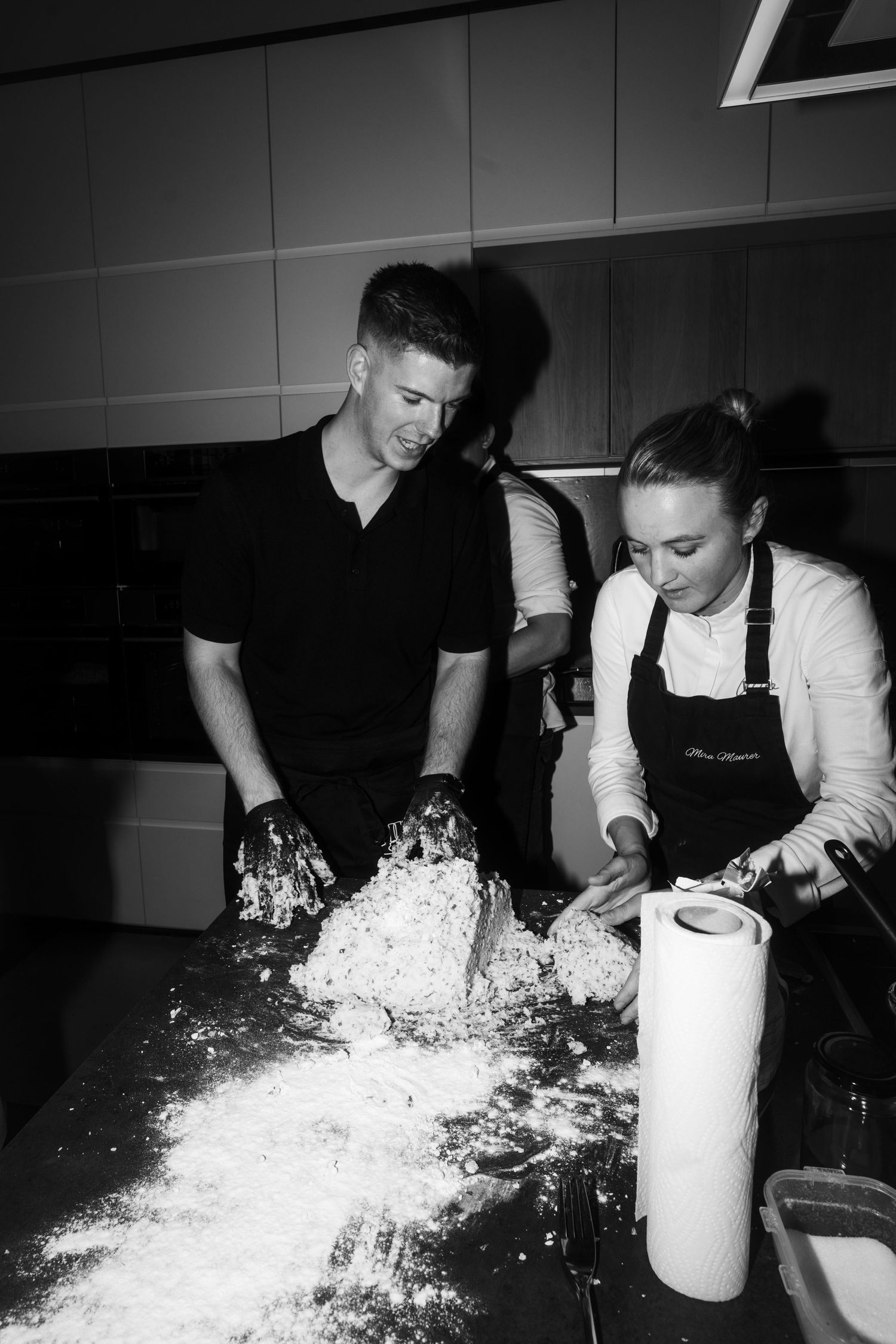 Two people working with flour and dough on a kitchen counter during food preparation.