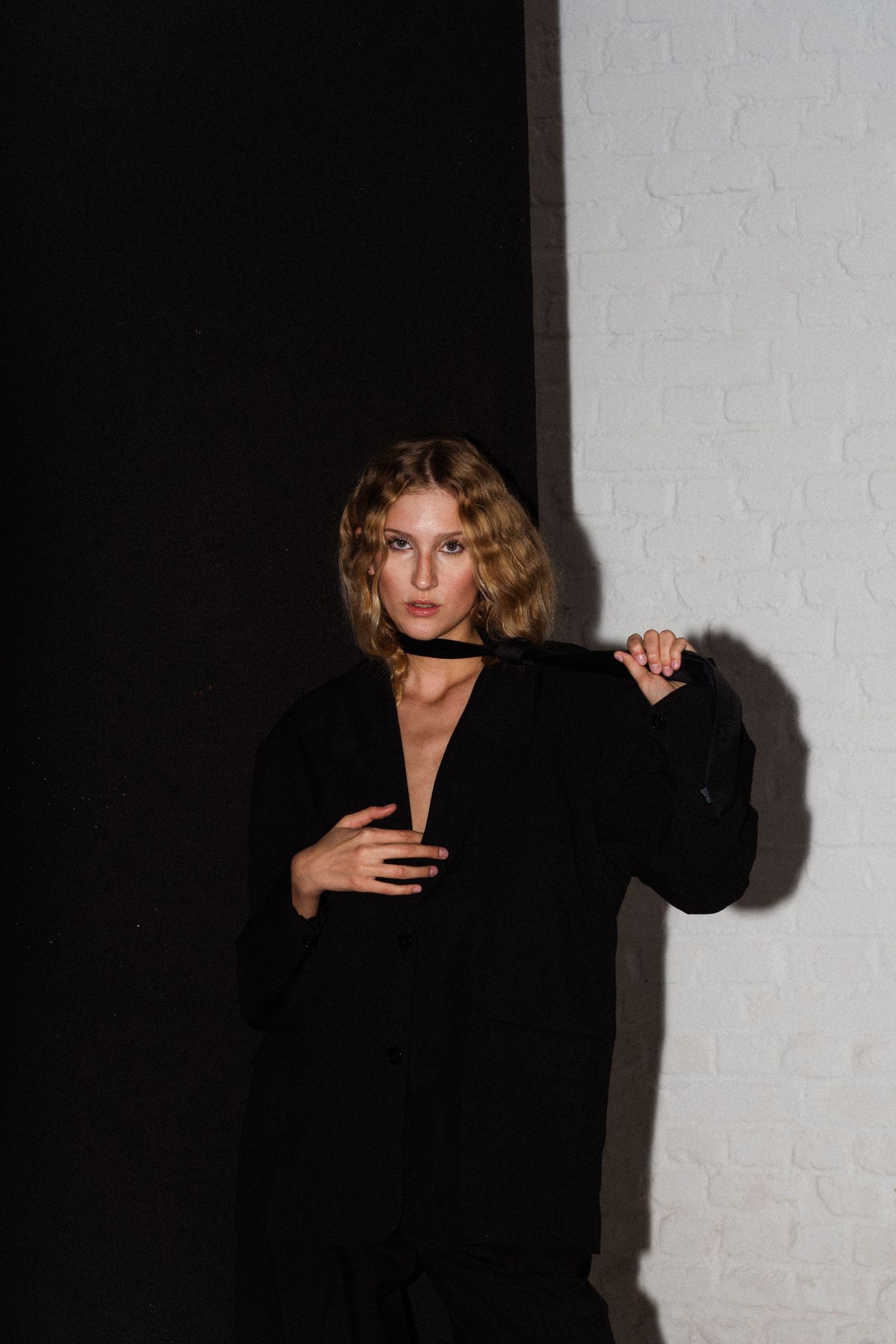 Dramatic portrait of someone in black attire against a white brick wall.