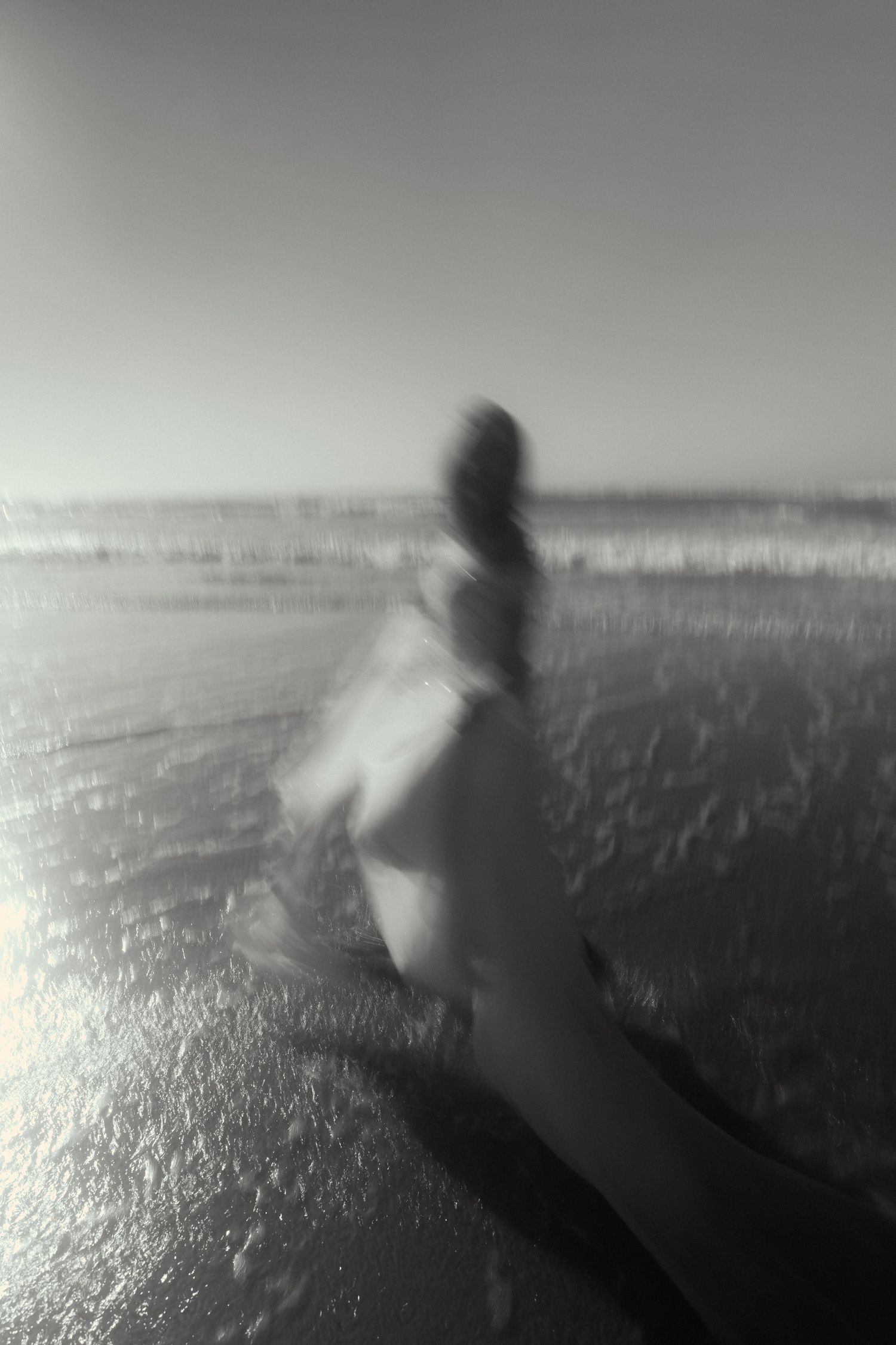 Atmospheric black and white image capturing movement on a reflective beach surface.