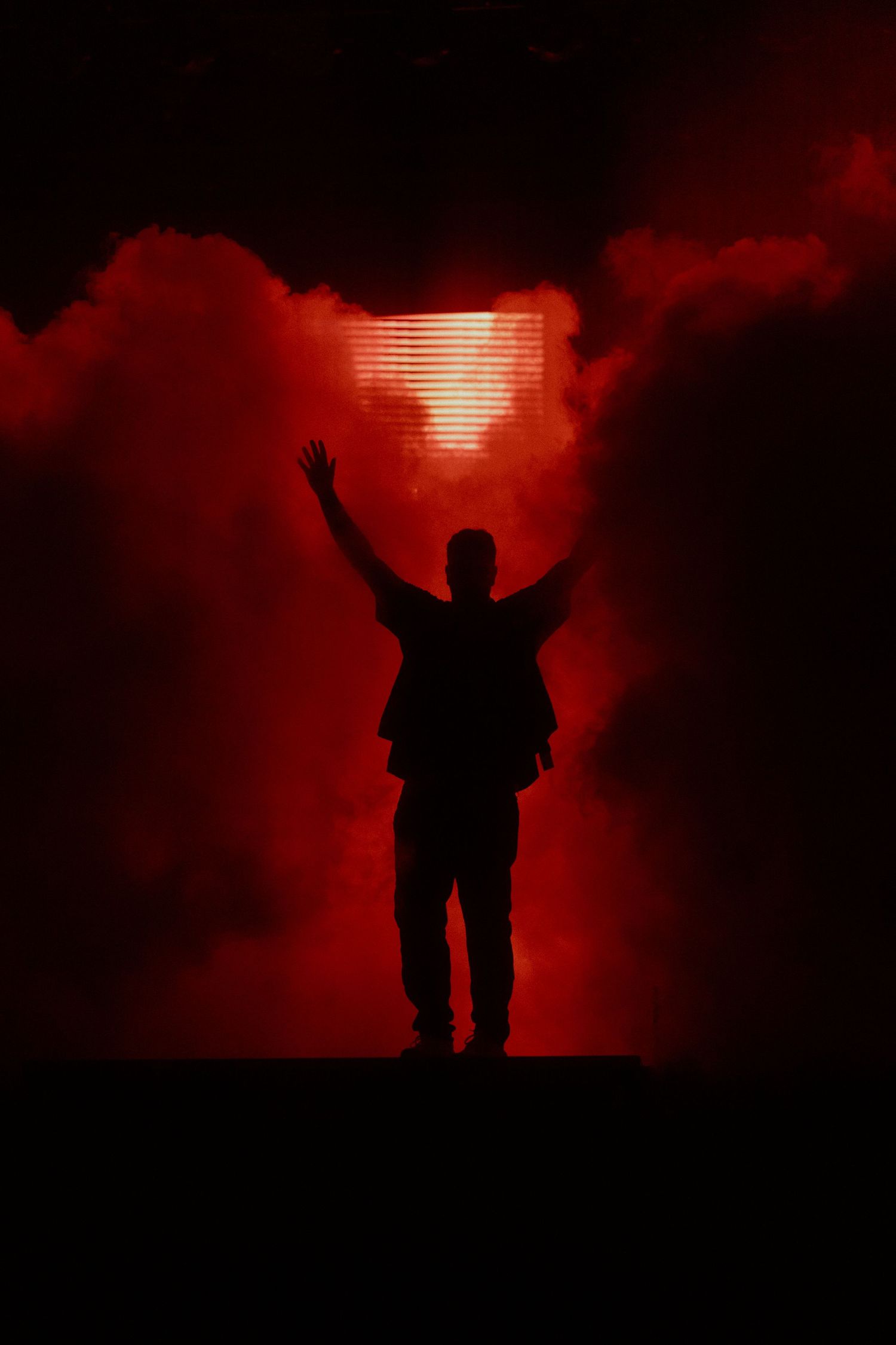 Silhouetted singer Marteria with raised arms against dramatic red lighting and smoke.