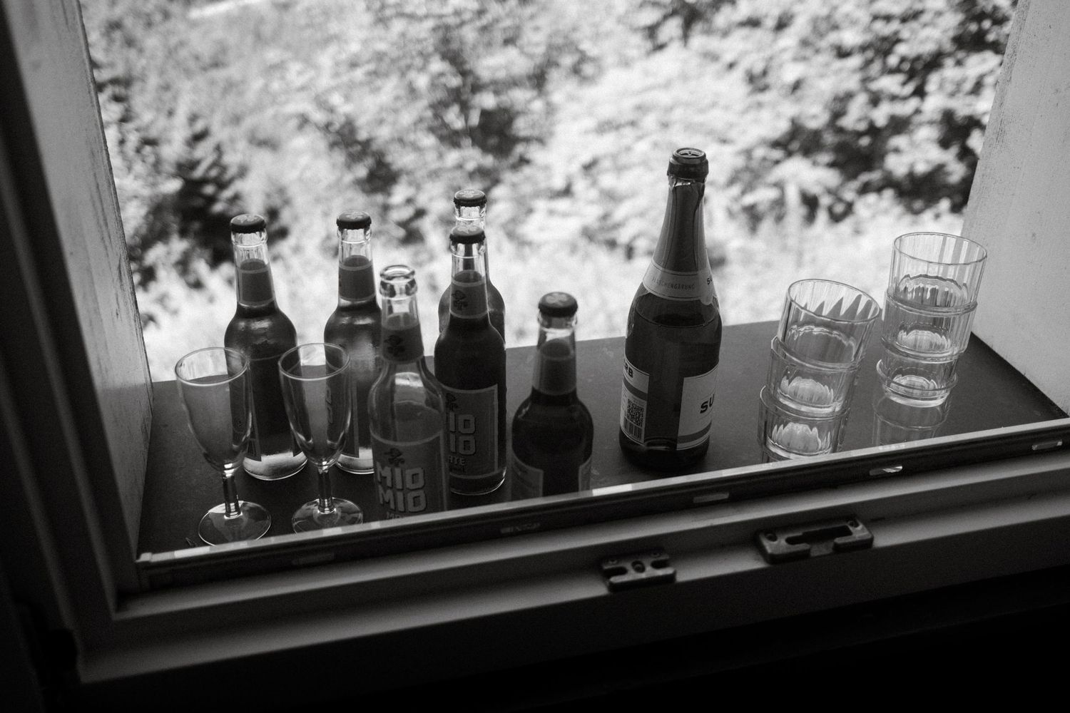 Row of glass bottles sits on a windowsill backlit by natural light creating a silhouette effect.