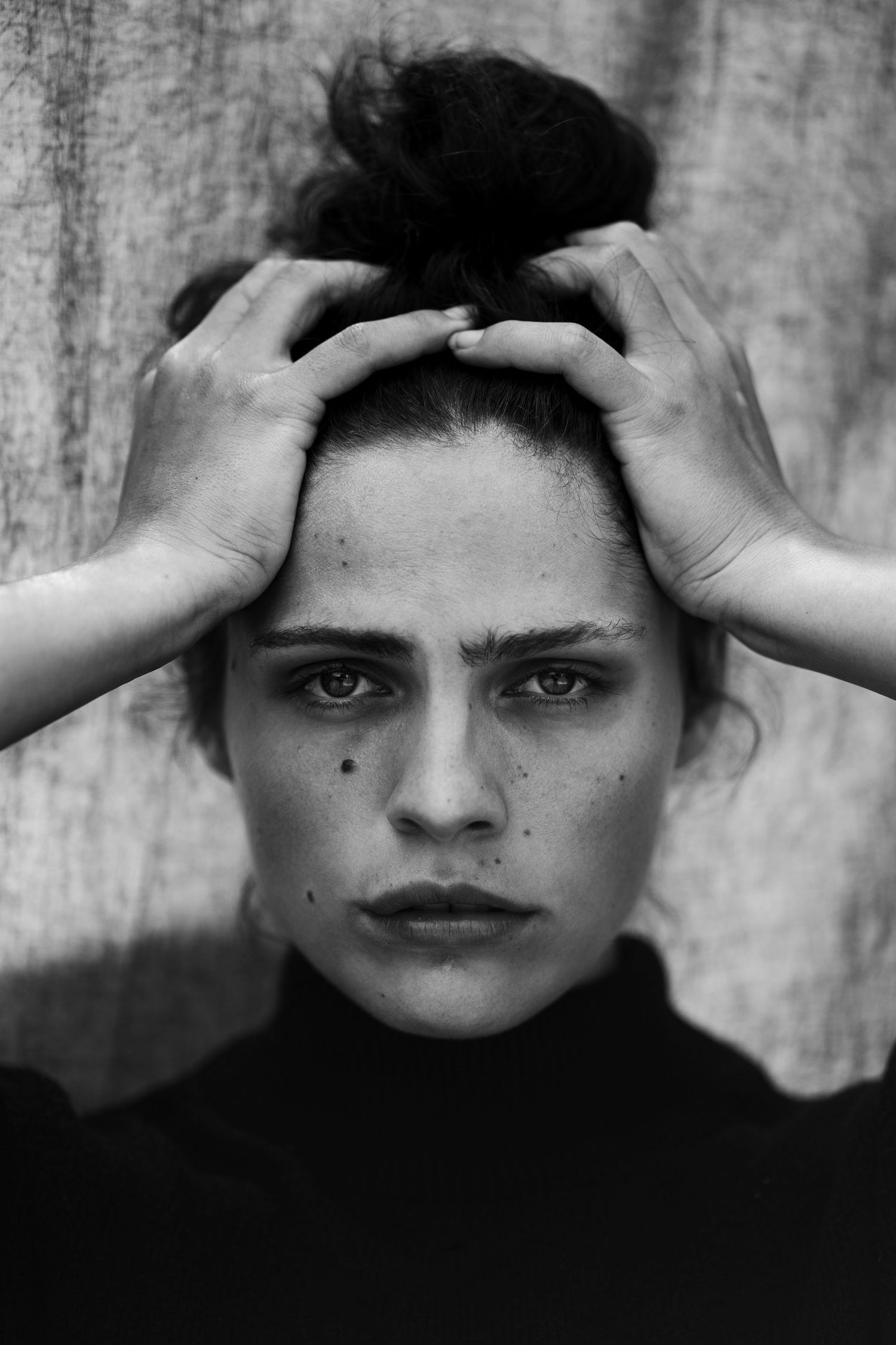 Black and white portrait with hands framing the composition against a textured background.