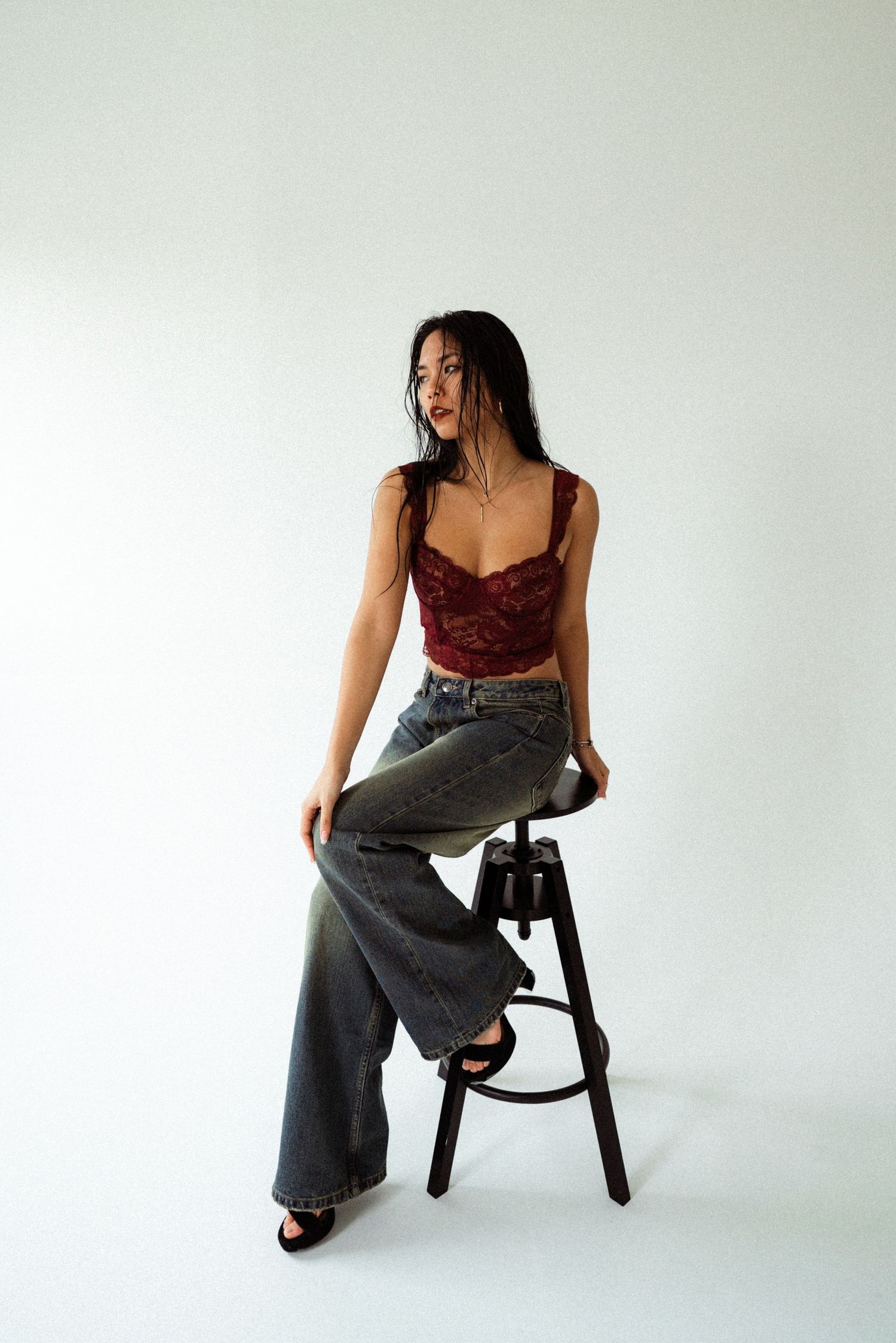 Casual fashion pose in burgundy top and relaxed denim against white background.