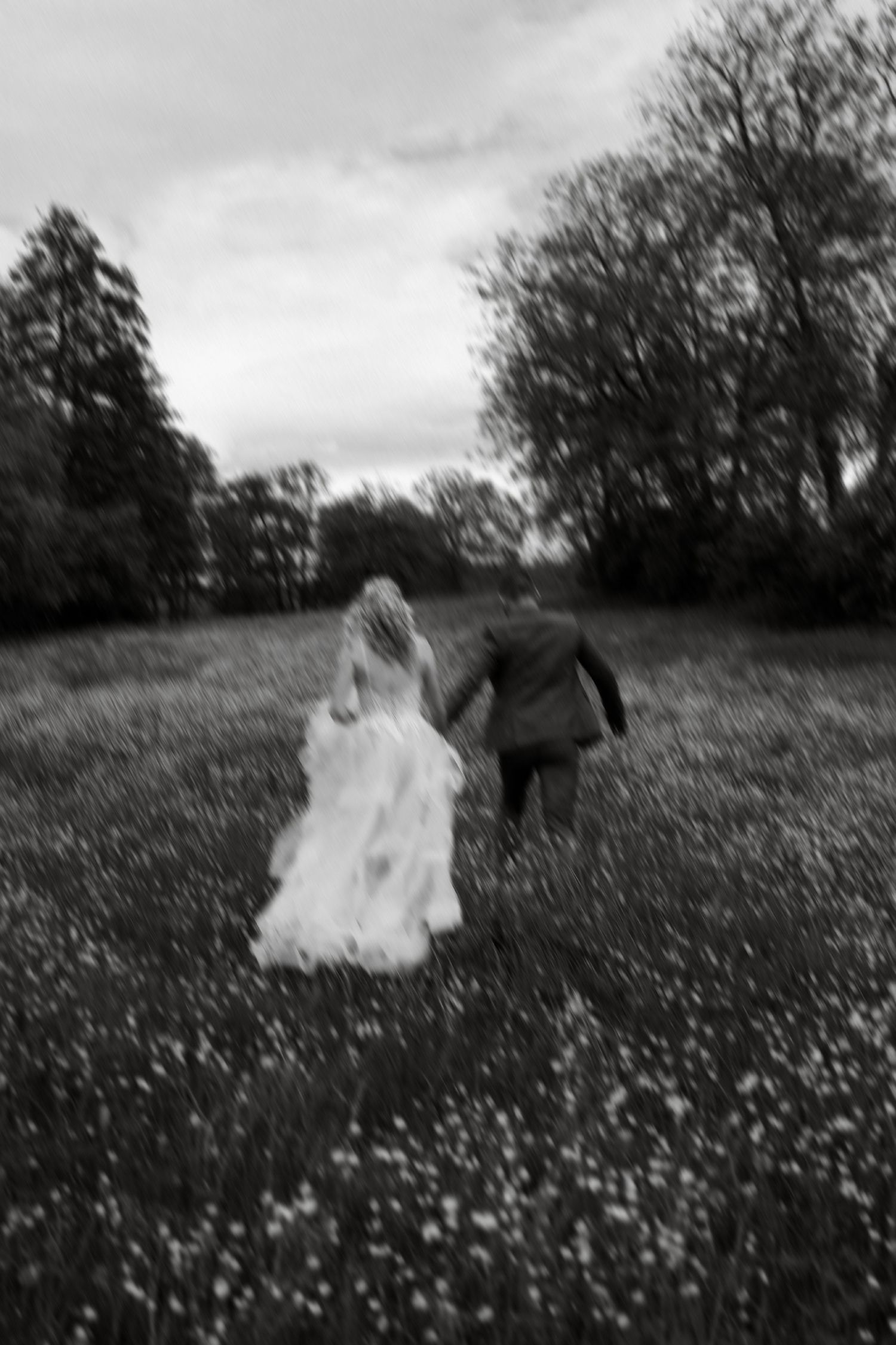 A black and white photo shows a couple walking through a flower-filled meadow, with the bride in a flowing white dress.
